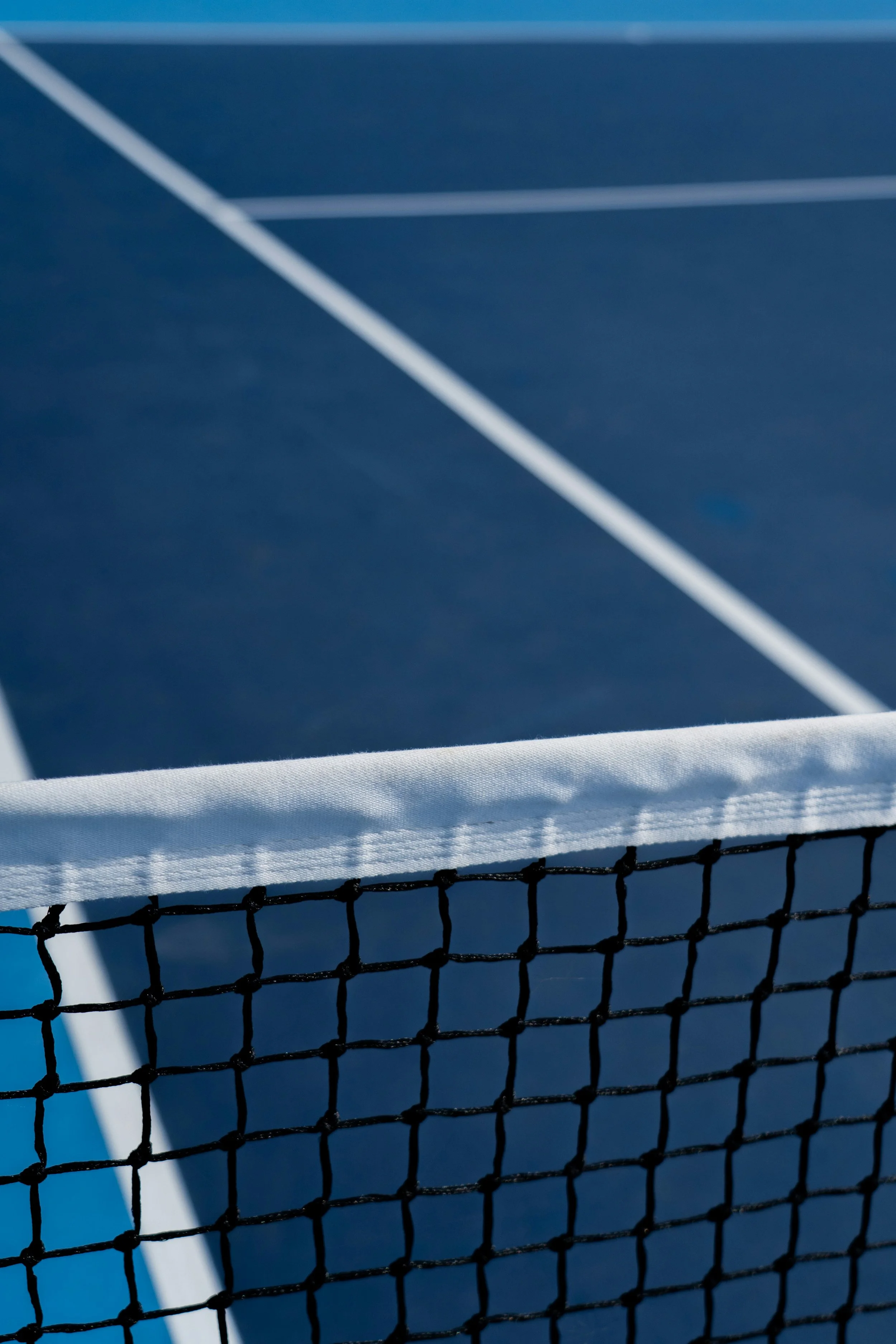 Close-up of a tennis net on a tennis court, with a section of the court surface visible in the background.