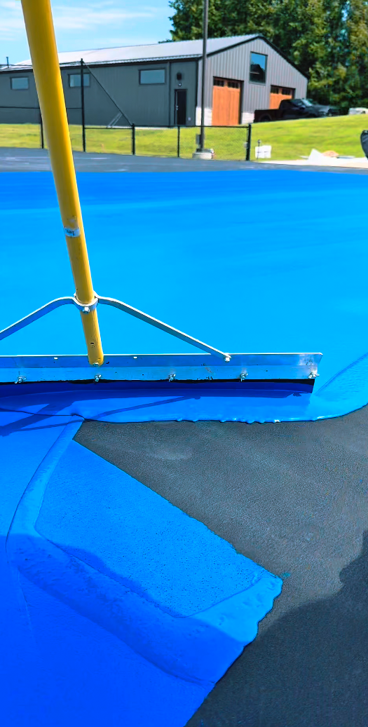 Close-up of a blue trampoline surface with a yellow pole and metal support connected to a black and gray safety pad.
