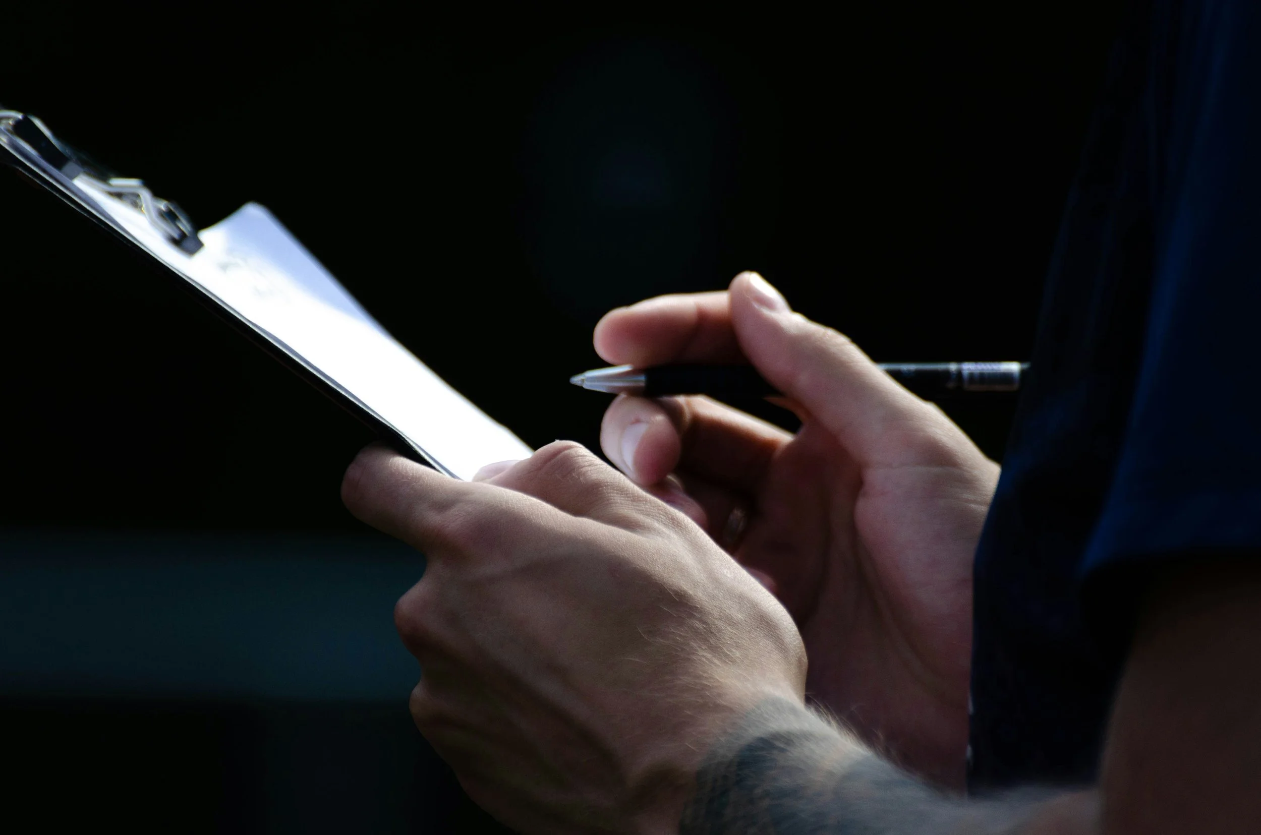 Close-up of a person holding a smartphone and writing with a pen, with a dark background.