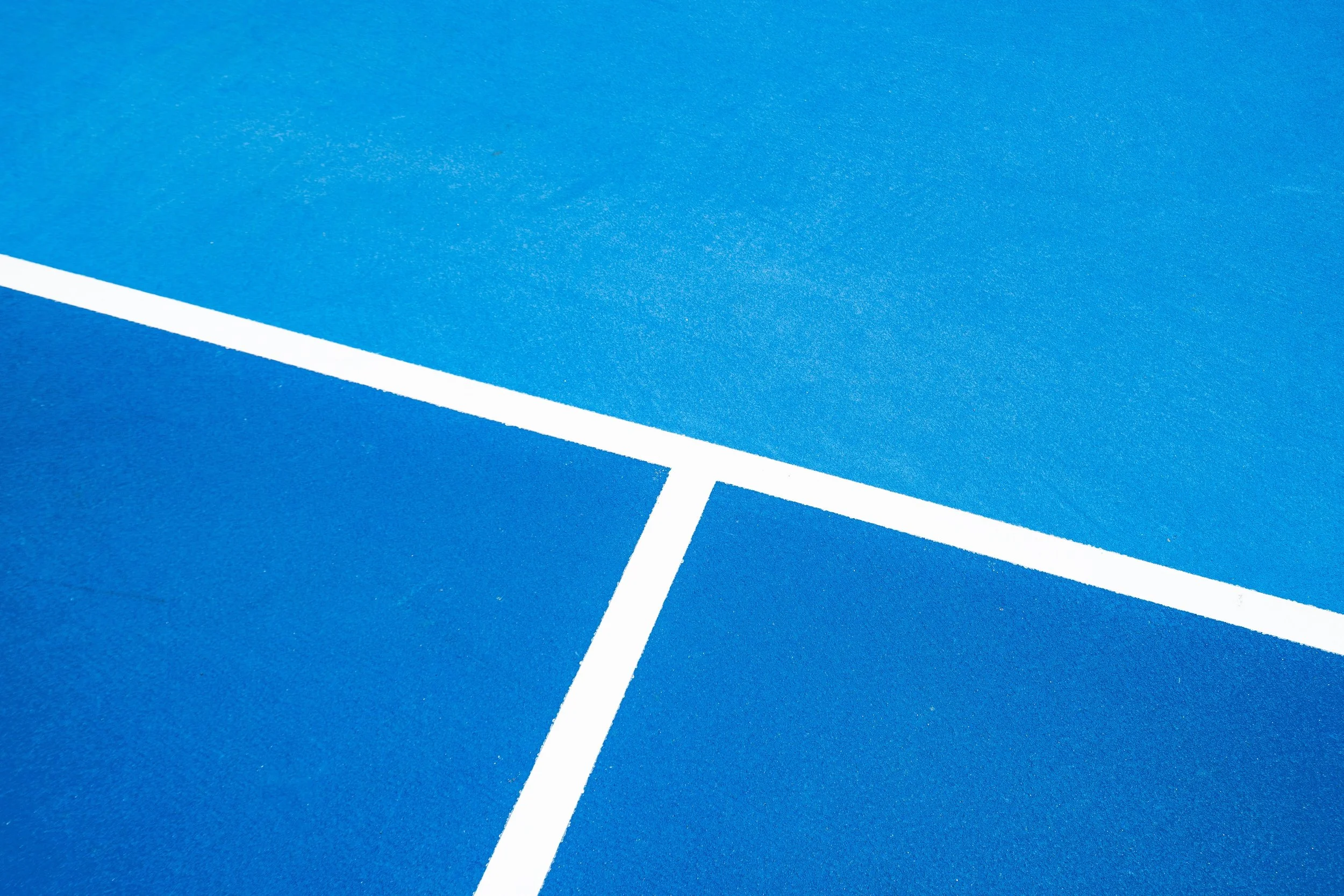 Close-up of a blue tennis court with white lines.