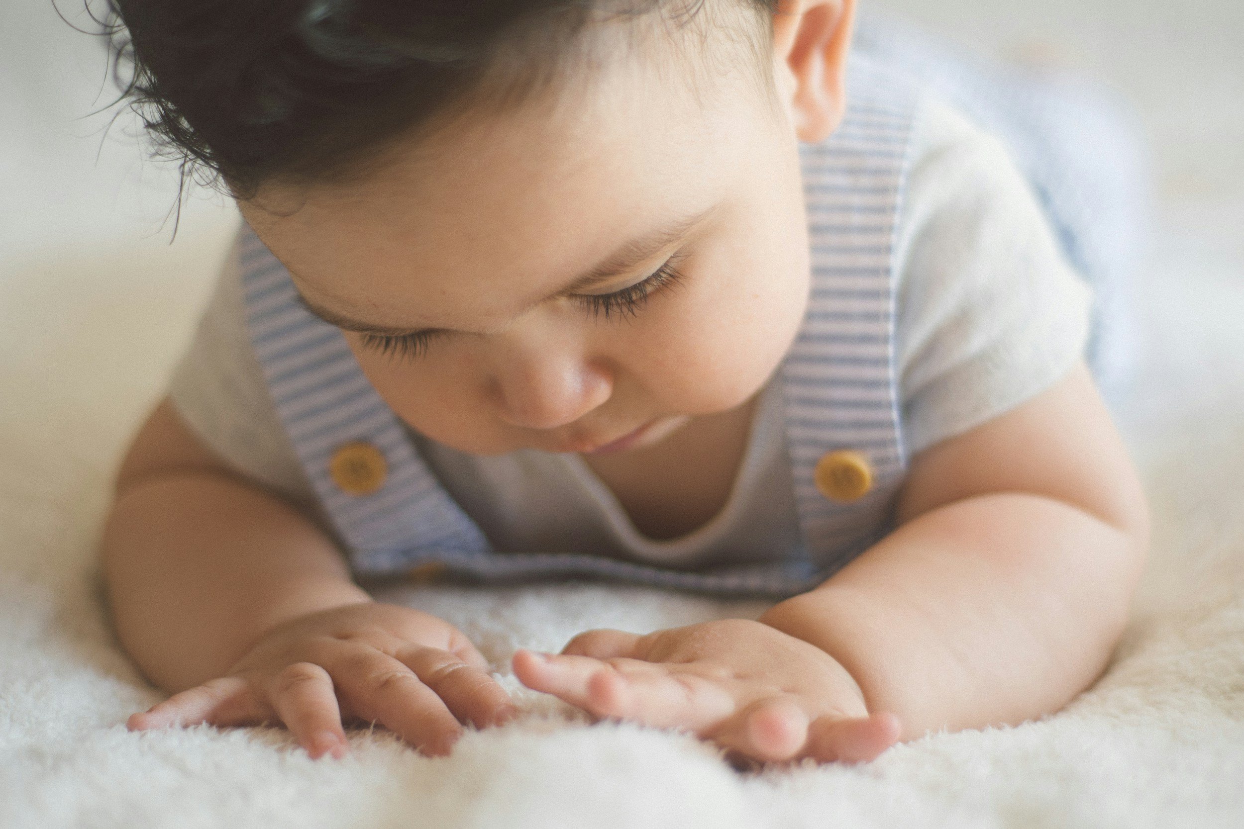 Baby in Bauchlage guckt Hände an