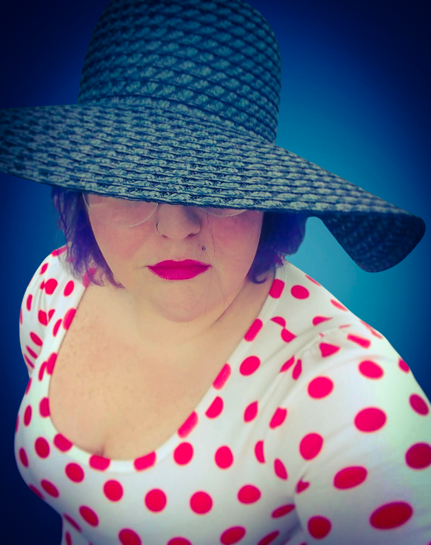 A woman wearing a large, wide-brimmed hat that covers her eyes, a white top with red polka dots, and bright pink lipstick, against a dark blue background.