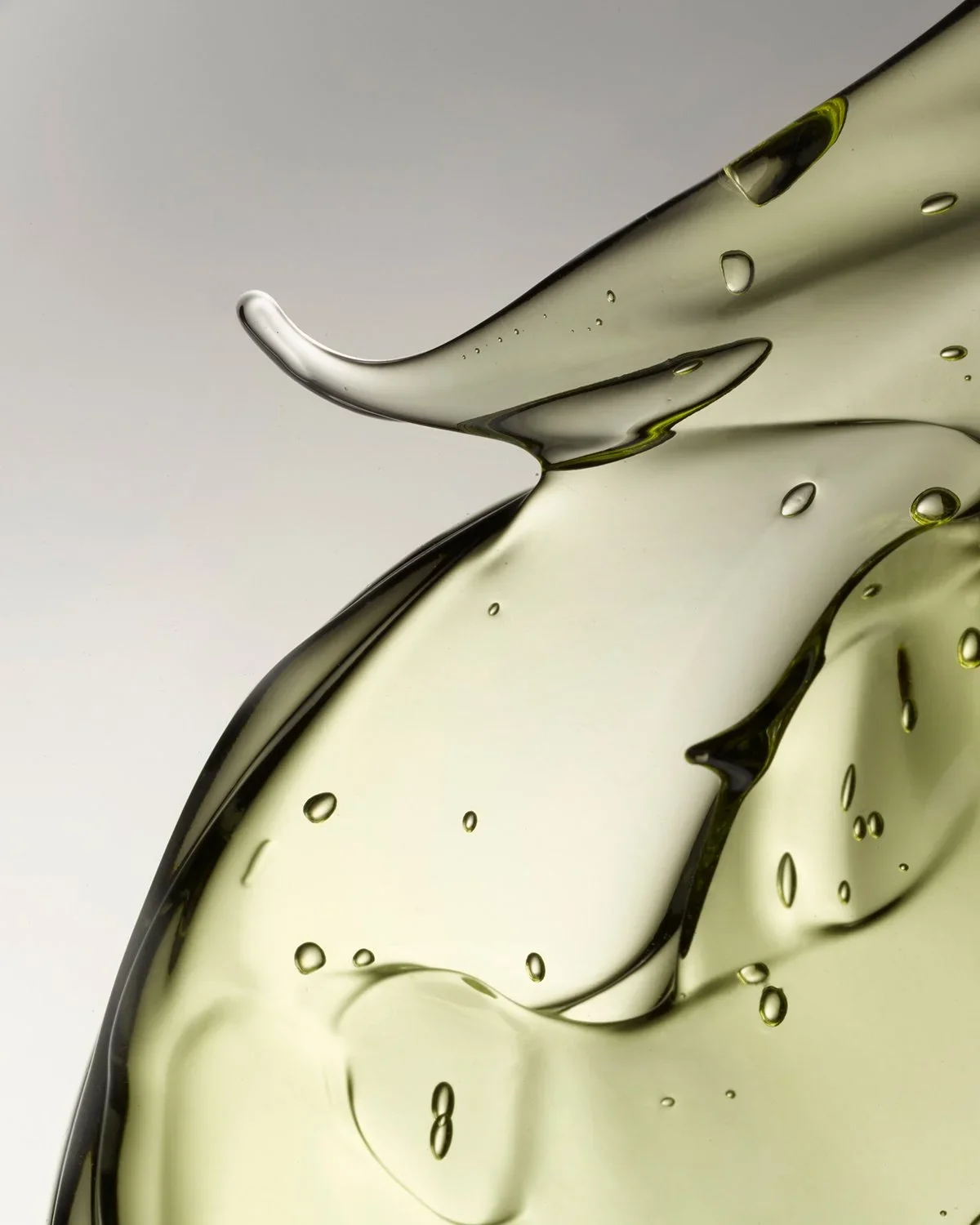 Close-up of clear liquid with bubbles, possibly oil or water, on a neutral background.