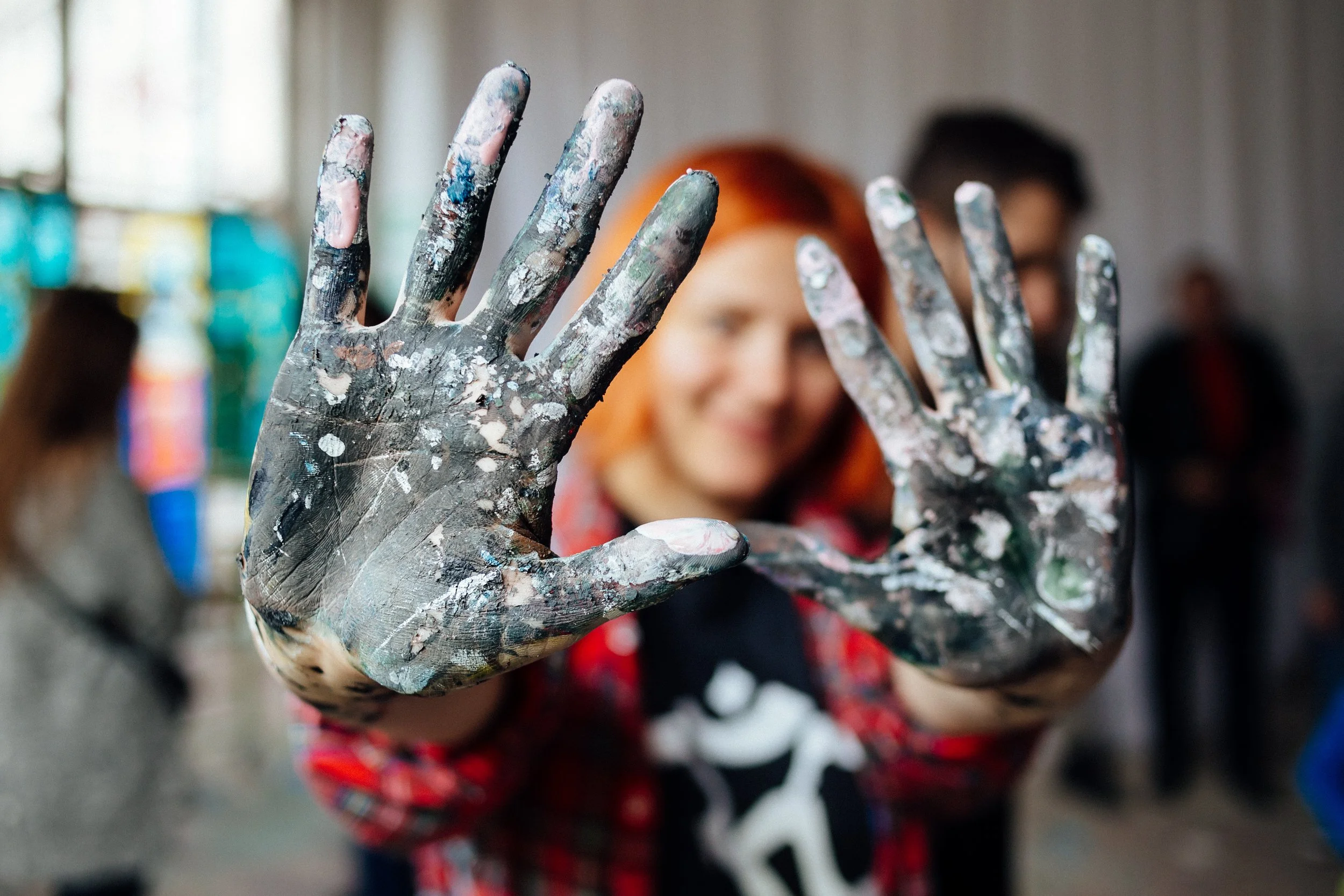Close-up of a person's hand covered in dried paint, with fingers spread apart, in a creative or artistic setting.