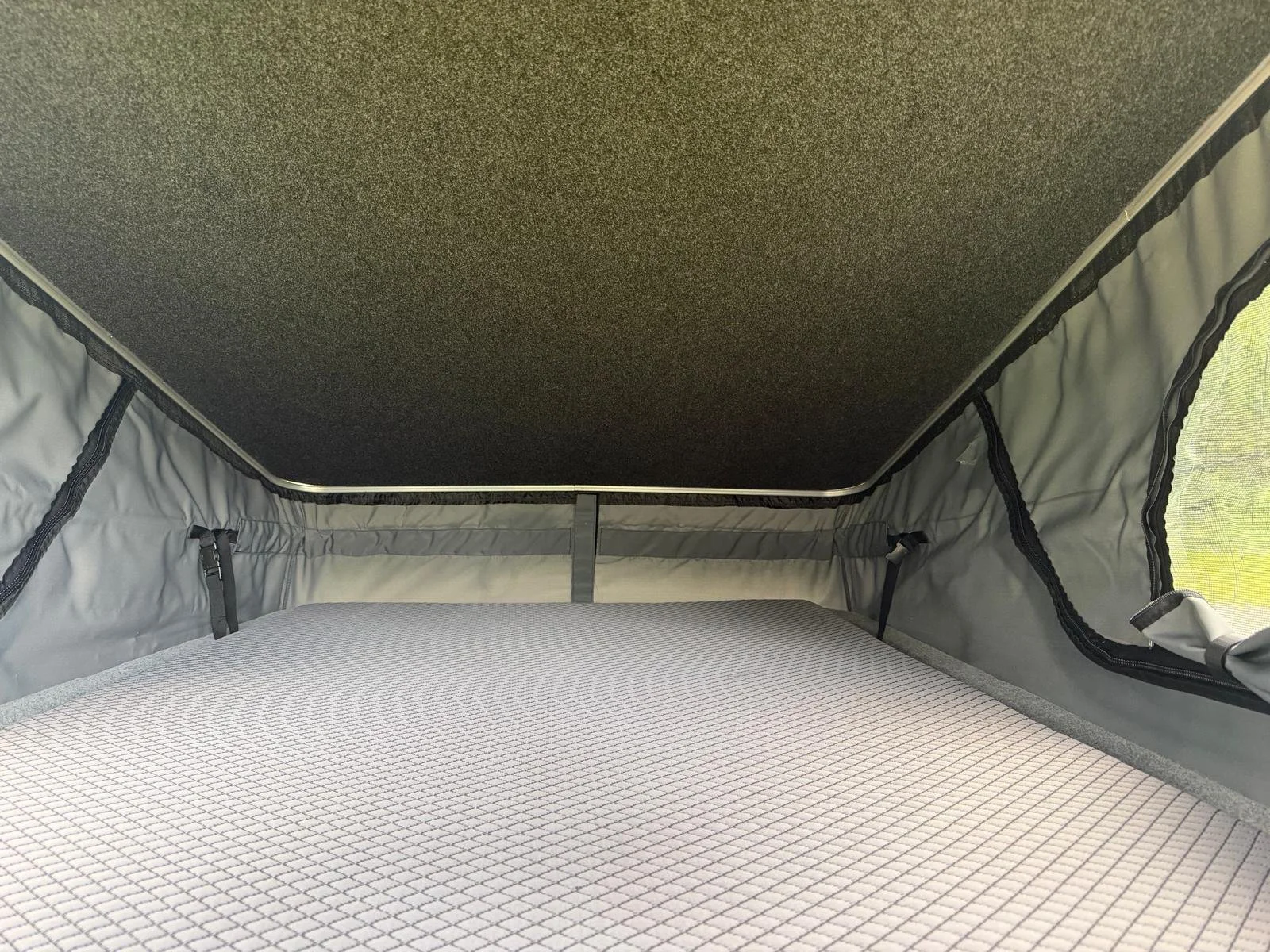 Empty bed inside a pop-up camper with window screens on the sides.