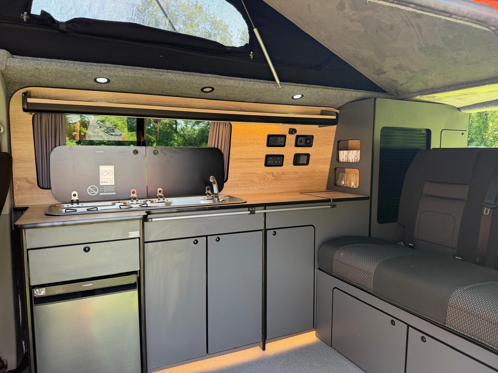 Interior of a converted camper van with a seating area, small table, wood paneling, and various electrical outlets and controls.