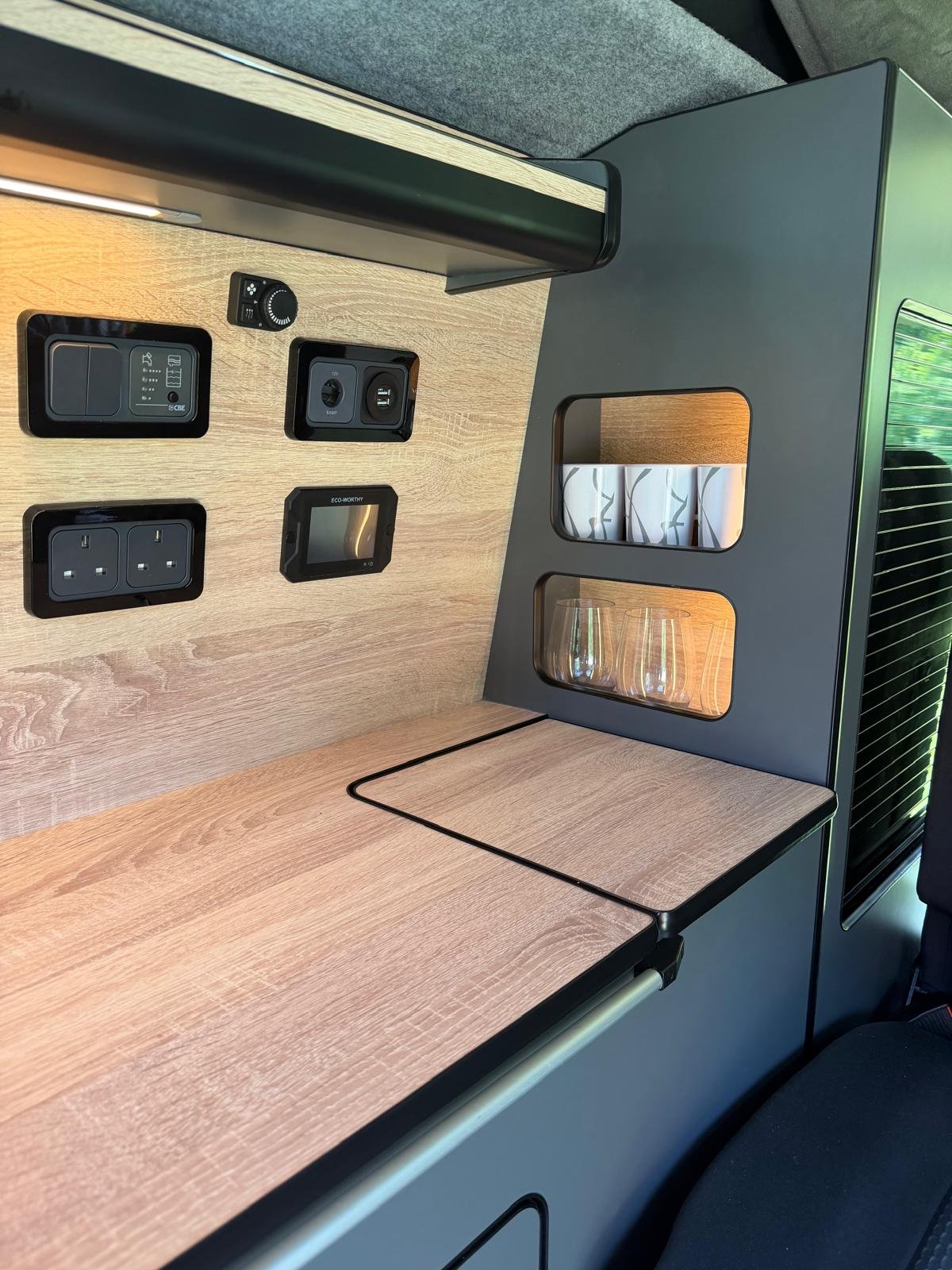 Close-up of a built-in power outlet, USB port, and glass holders in a modern, wooden interior space.