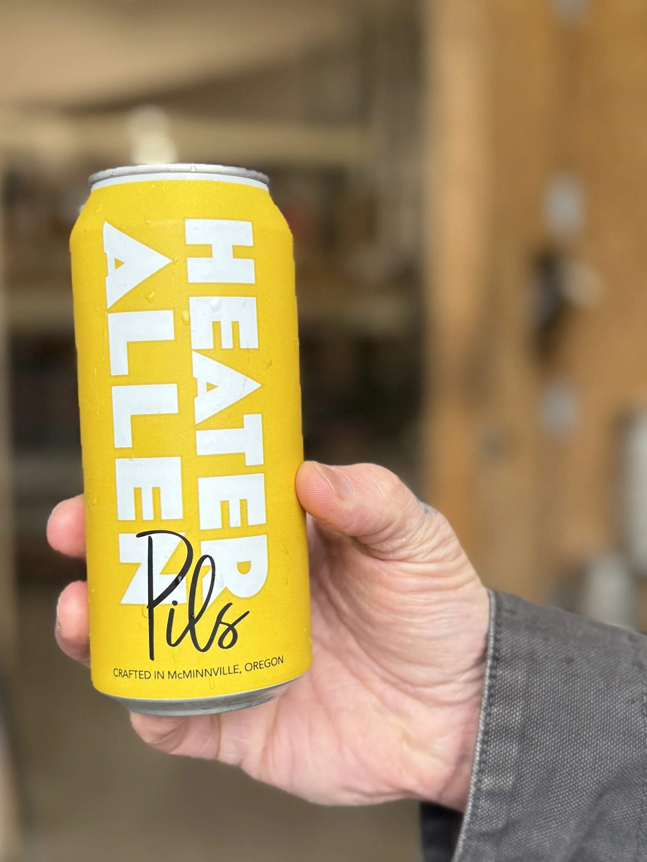 A person holding a yellow can of Heater Allen Pils, a beer from McMinnville, Oregon.