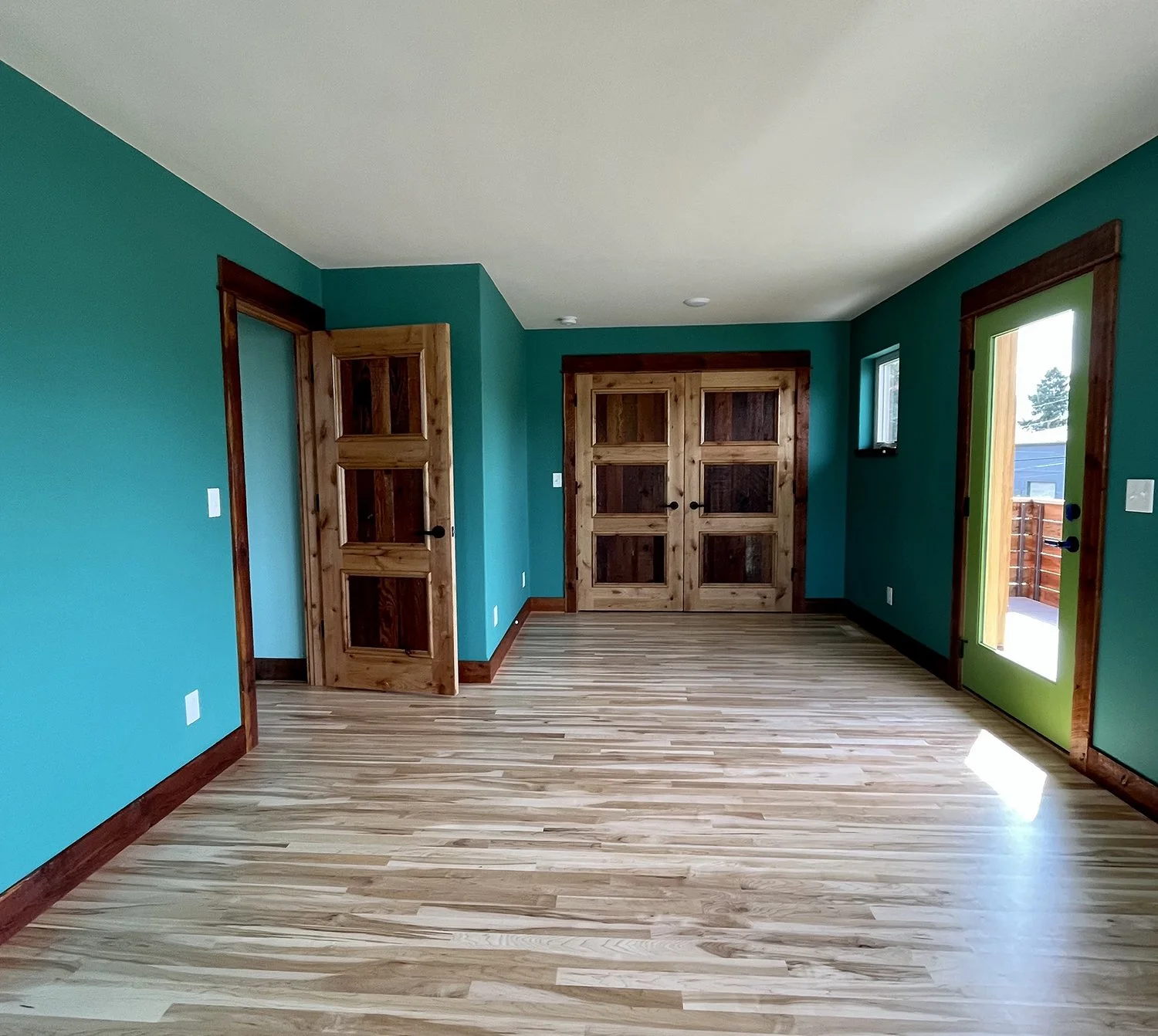 Empty room with teal walls, wooden trim, hardwood floor, and wooden doors, including a sliding door leading outside.