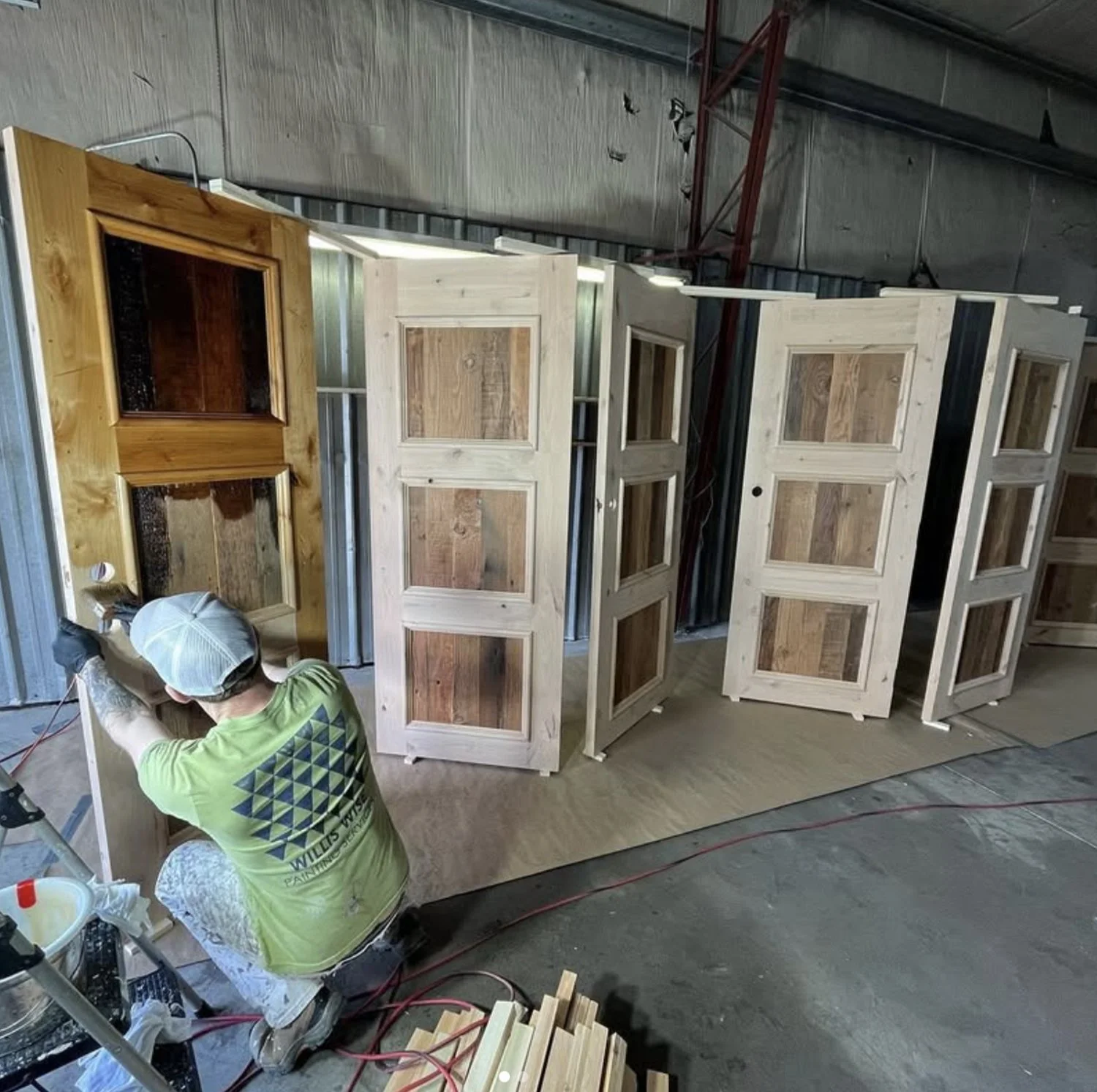 A person working on wooden window frames in a workshop with metal walls and overhead lighting.