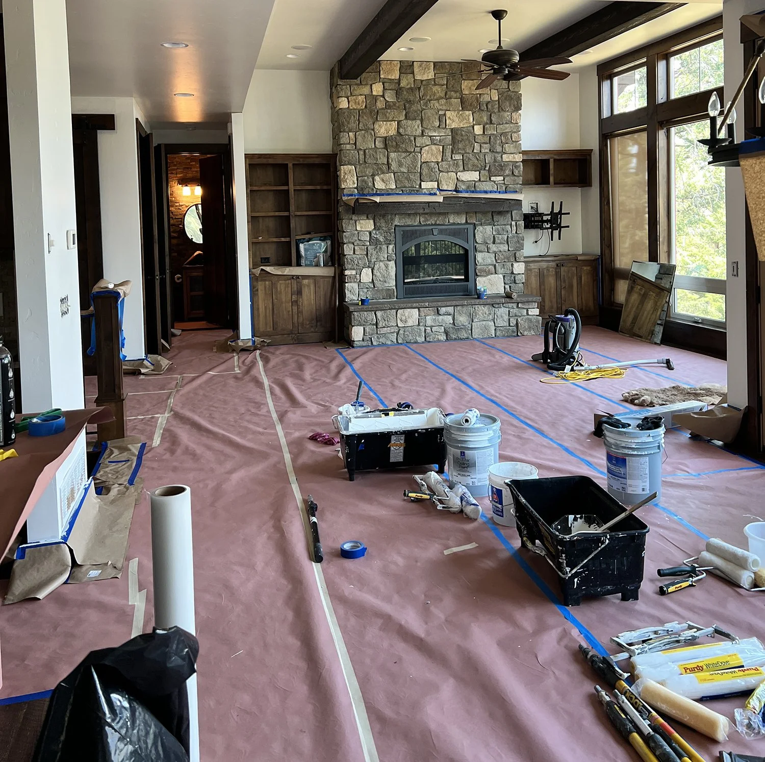Living room under renovation with pink protective floor covering, construction tools and materials, and a stone fireplace.