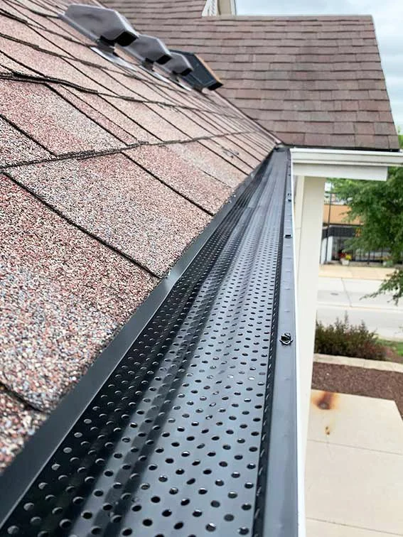 Close-up view of a roof with asphalt shingles and a black metal gutter guards to keep home dry and safe by National Roofing St. Louis area