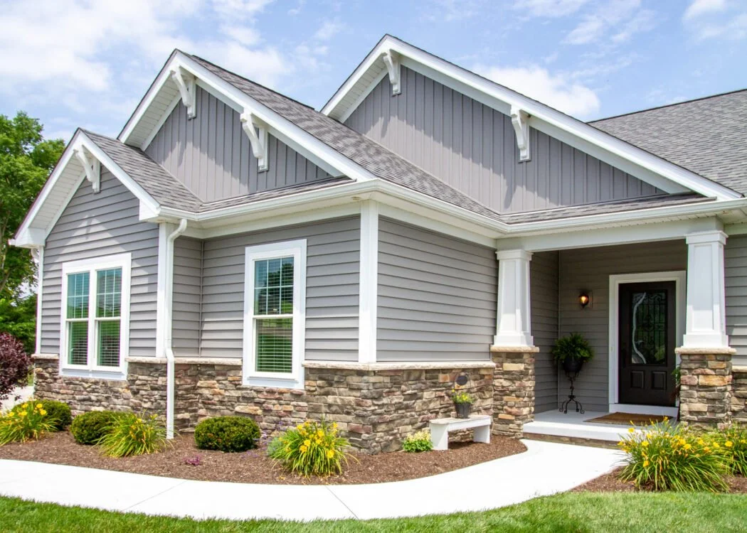 Front view of a modern house with gray siding, stone accents, white trim, and a covered porch with a black door.