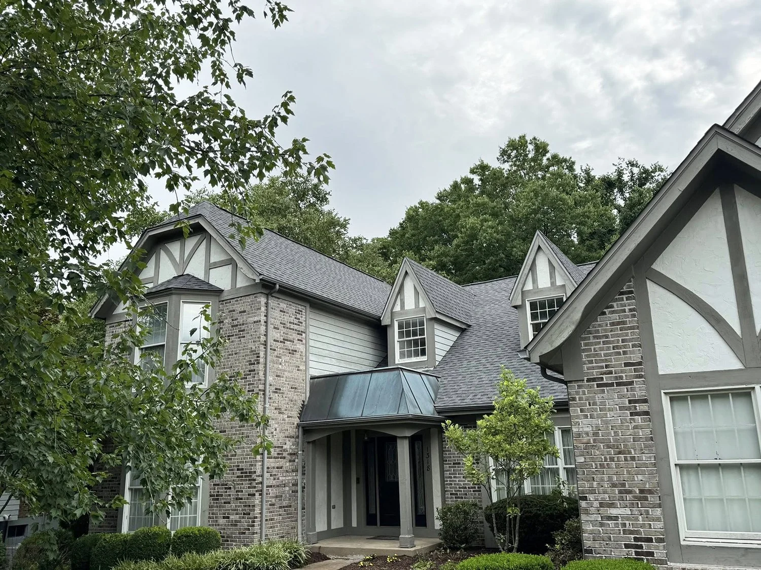 Residential home with roof replacement by National Roofing St. Louis and brick and white siding exterior, multiple gabled roofs, and bay windows, surrounded by trees and a landscaped front yard.
