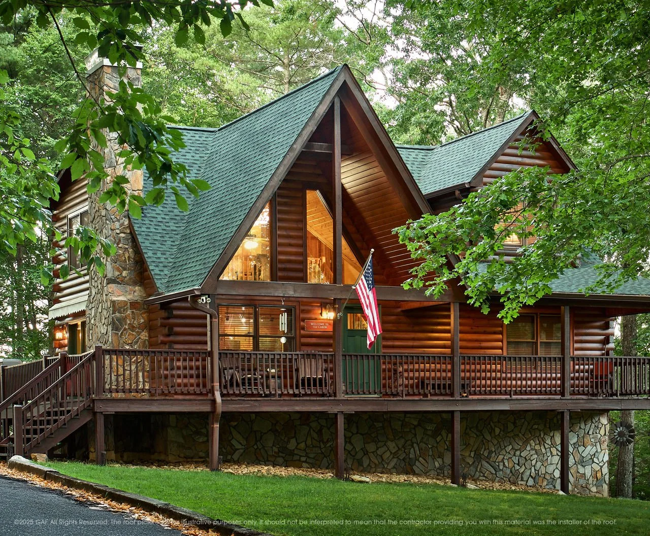 A large wooden house with a steep green roof by National Roofing St. Louis with a stone chimney, and expansive deck in a wooded area with trees and green grass.