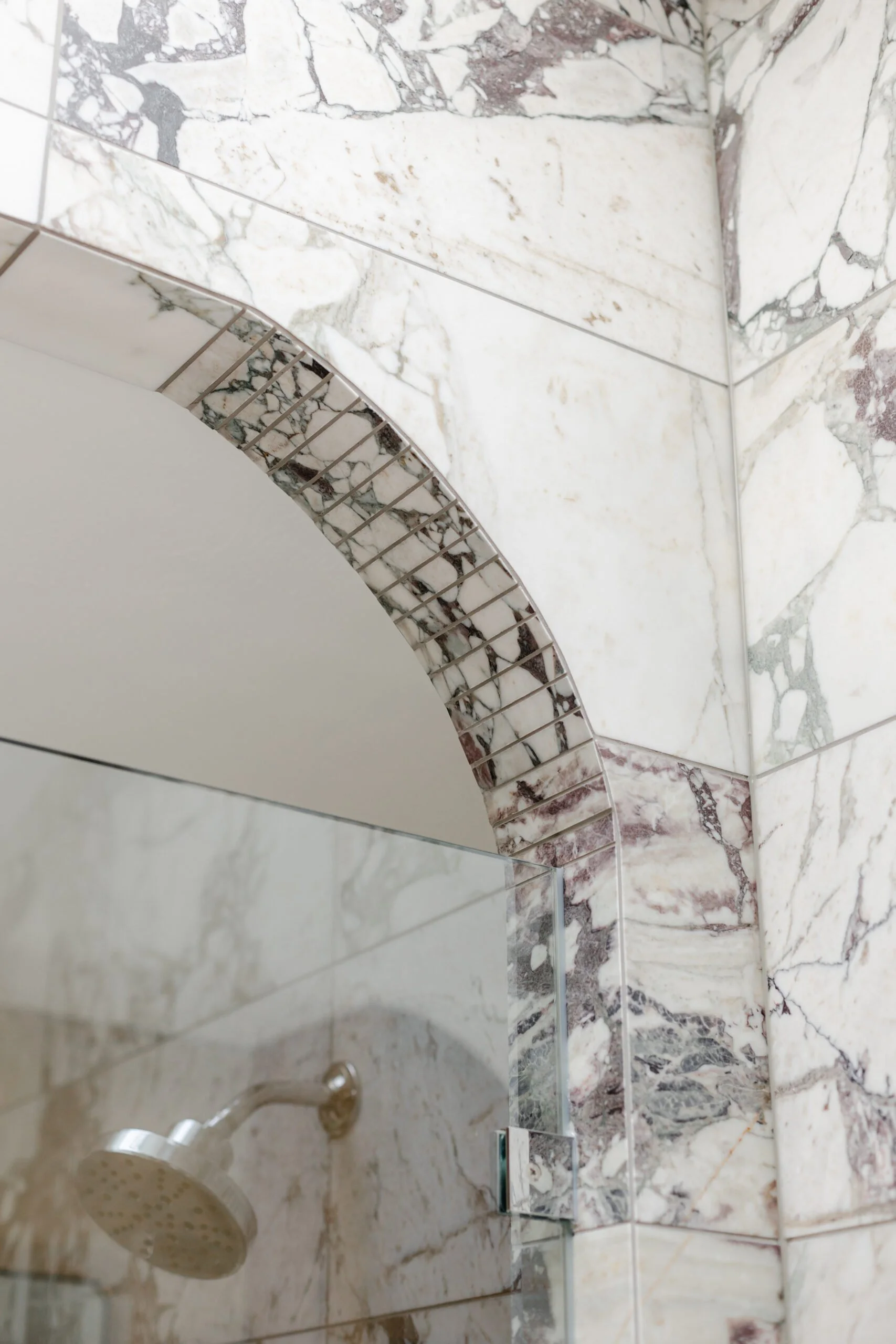 White and grey marbled tiling in arched bathroom shower doorway by S Flynn Design + Build