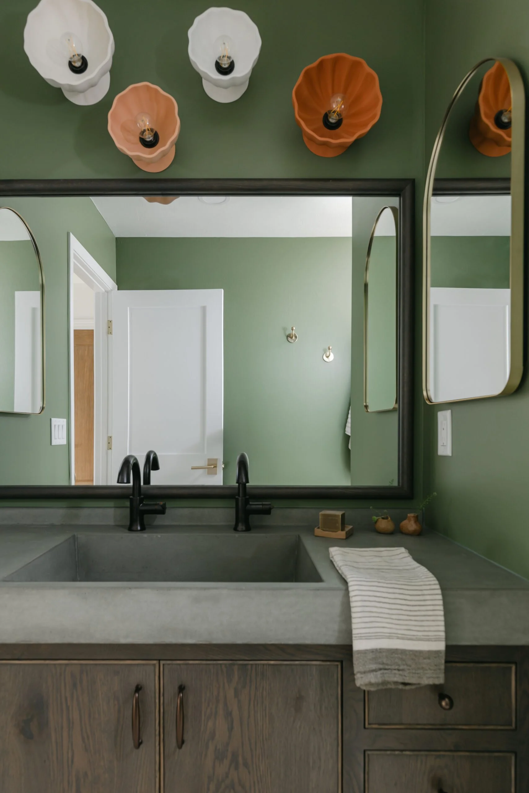 Dark brown wooden cabinets, colorful floral light fixtures, and sage green walls in bathroom remodel by S. Flynn Design + Build