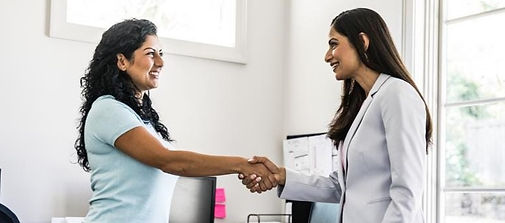 Two women smiling and shaking hands in an office setting.