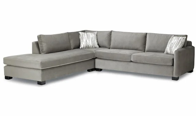 Light gray sectional sofa with a chaise lounge, two decorative pillows, and black block feet.