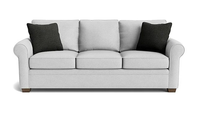 A white upholstered sofa with three seat cushions, rolled arms, and two black throw pillows against a plain white background.