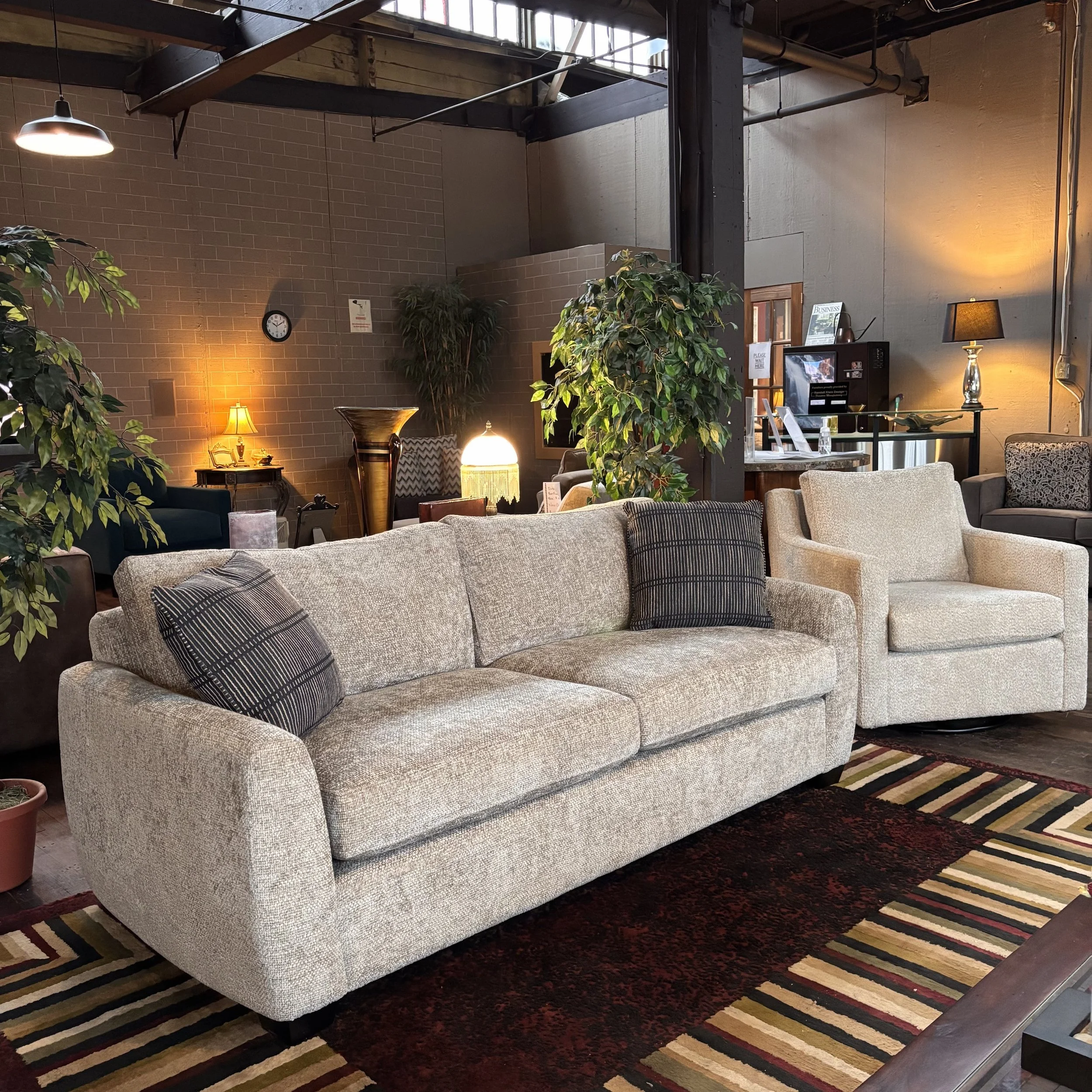 Indoor furniture store showing beige sofa with black-striped pillows, a beige armchair, and various lamps and plants in the background.