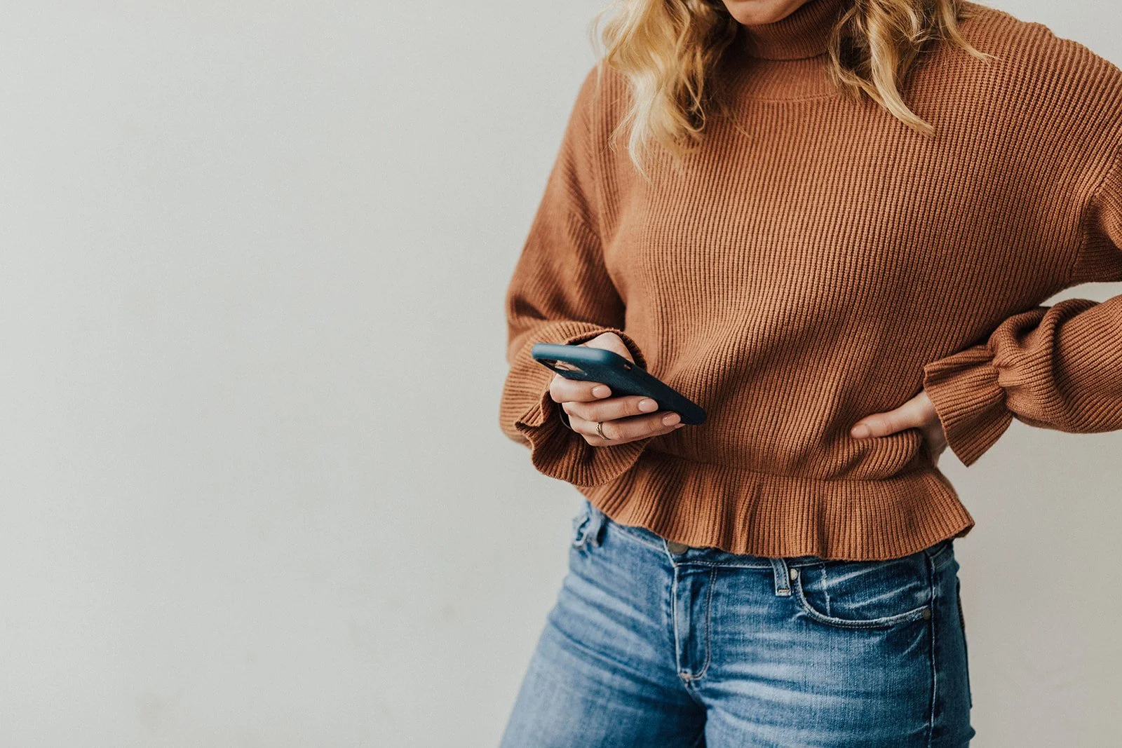 A woman wearing a brown sweater and jeans holding a smartphone.