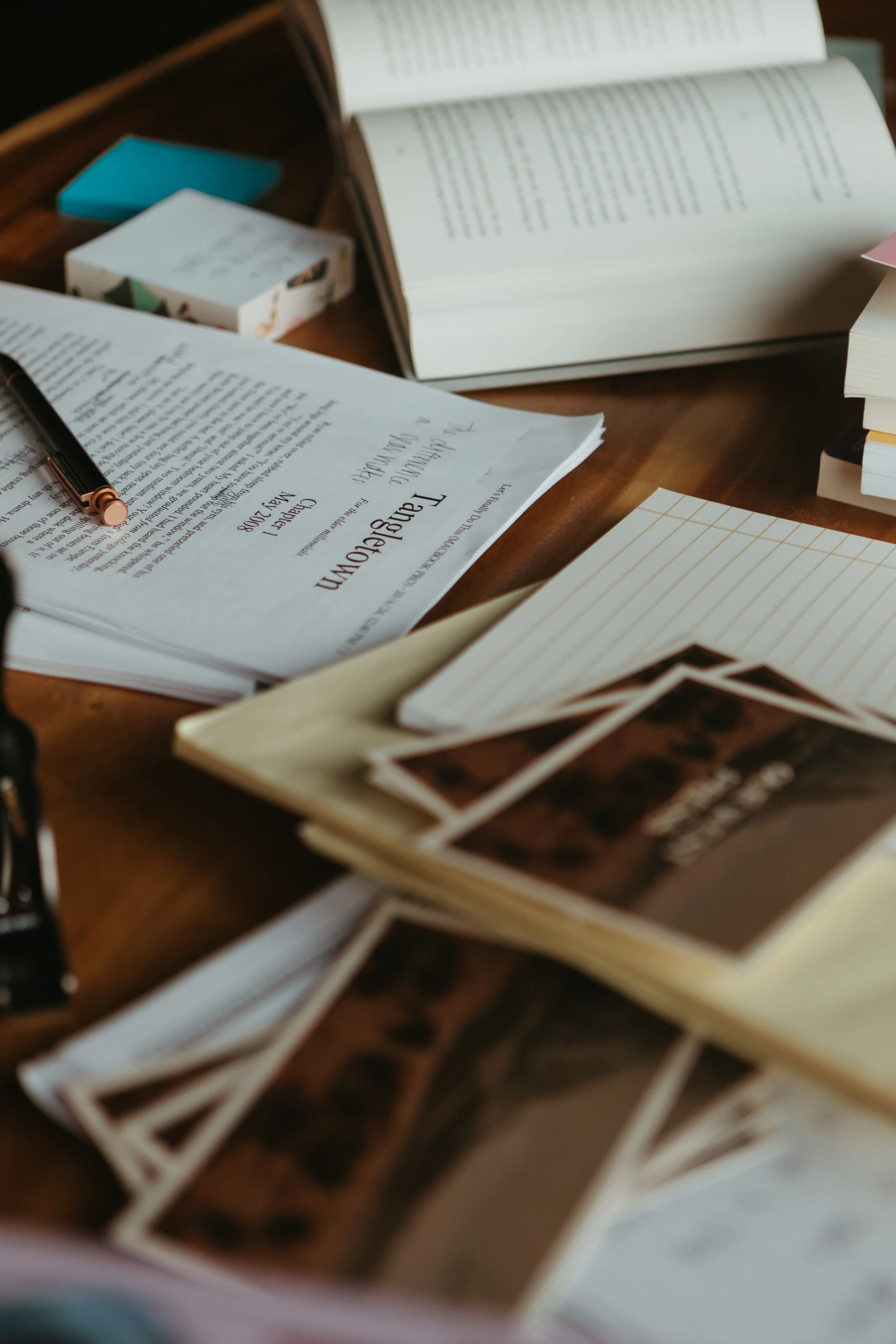 Open notebook and scattered printed photos or pages on a wooden table.