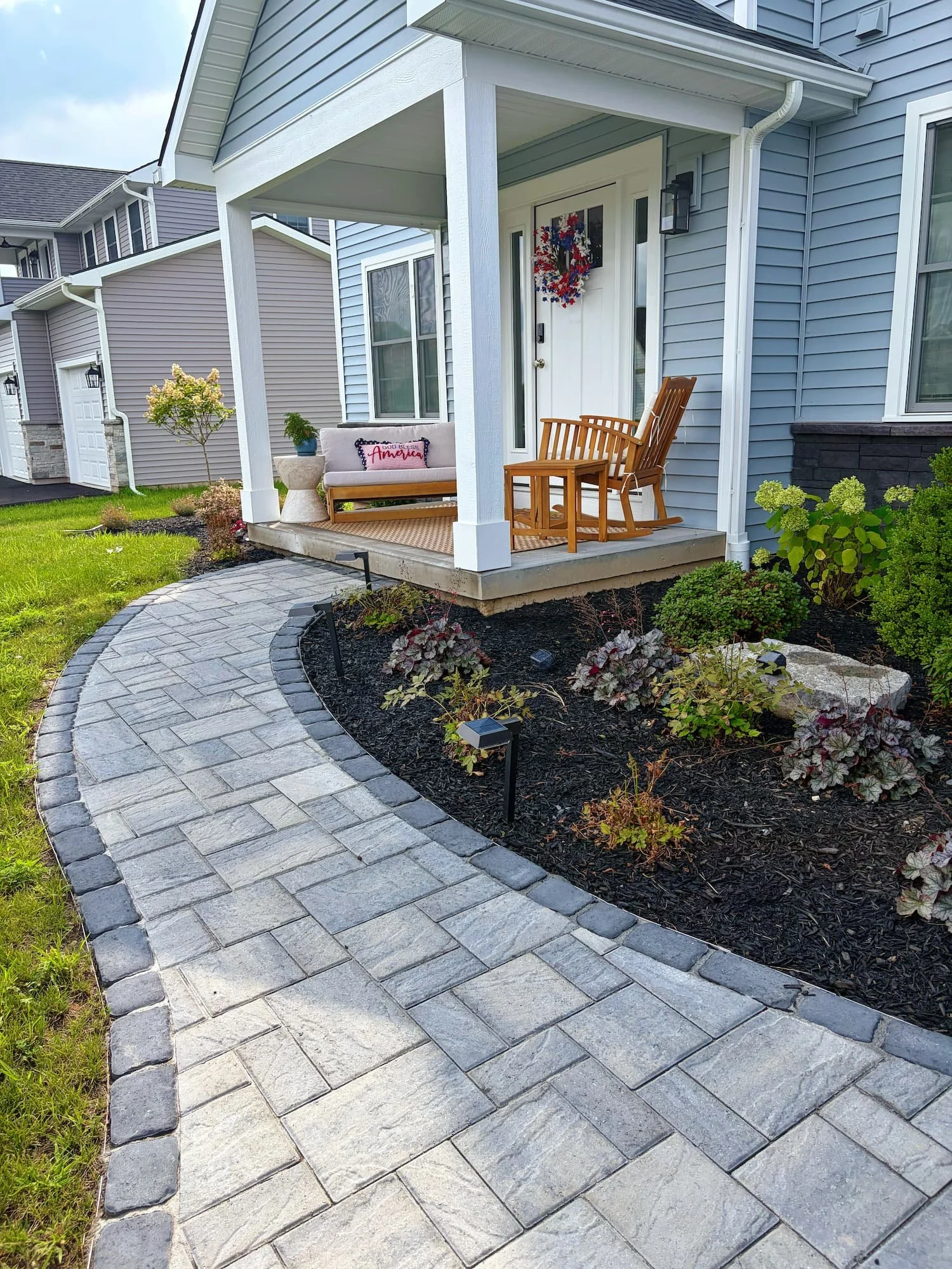 Completed residential front yard landscaping with planting beds and a paver walkway in Central NY.