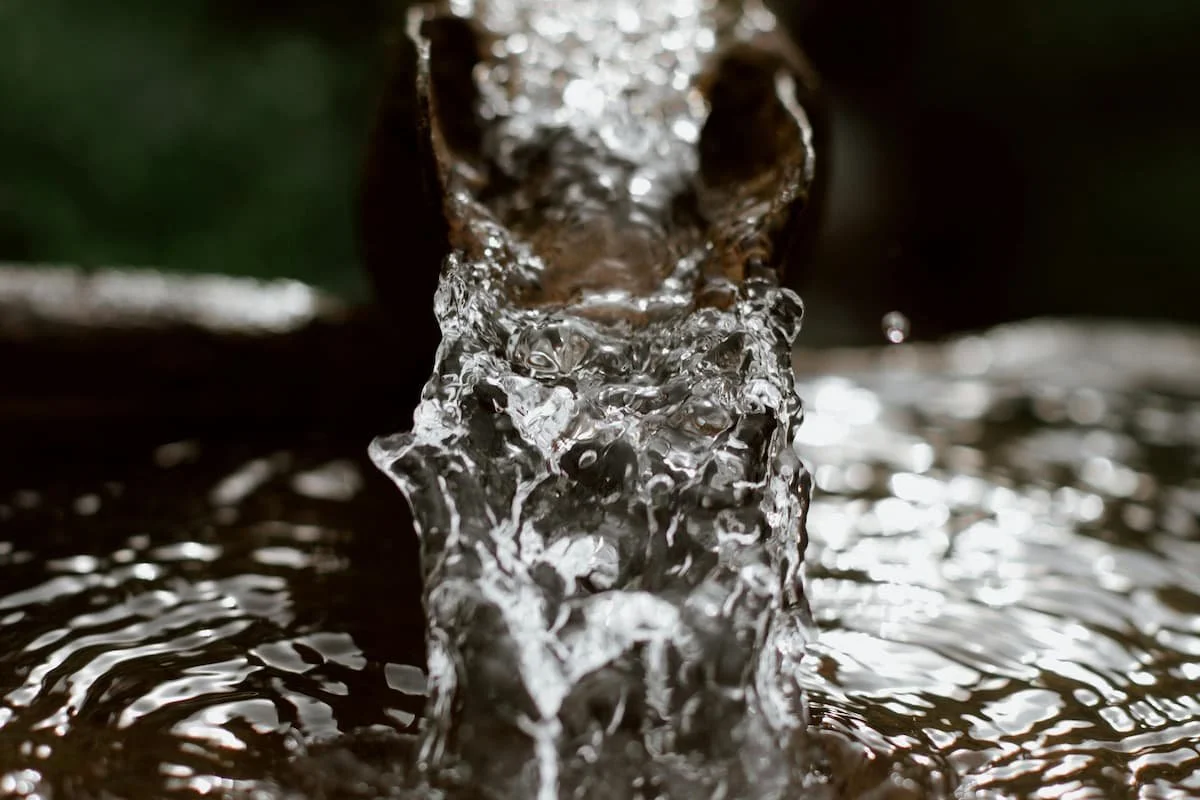 Close-up of flowing water splashing from a dark stone water feature with reflective ripples and dramatic lighting.