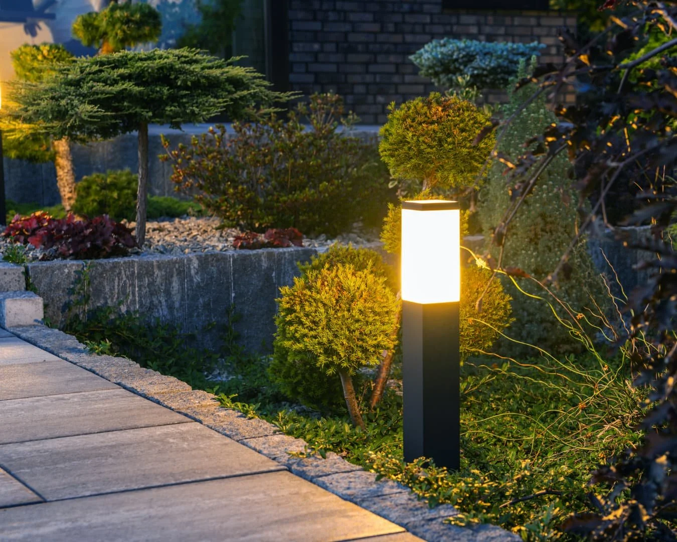 Outdoor lighting inspiration showing a warmly lit entry gate and stone path at night.