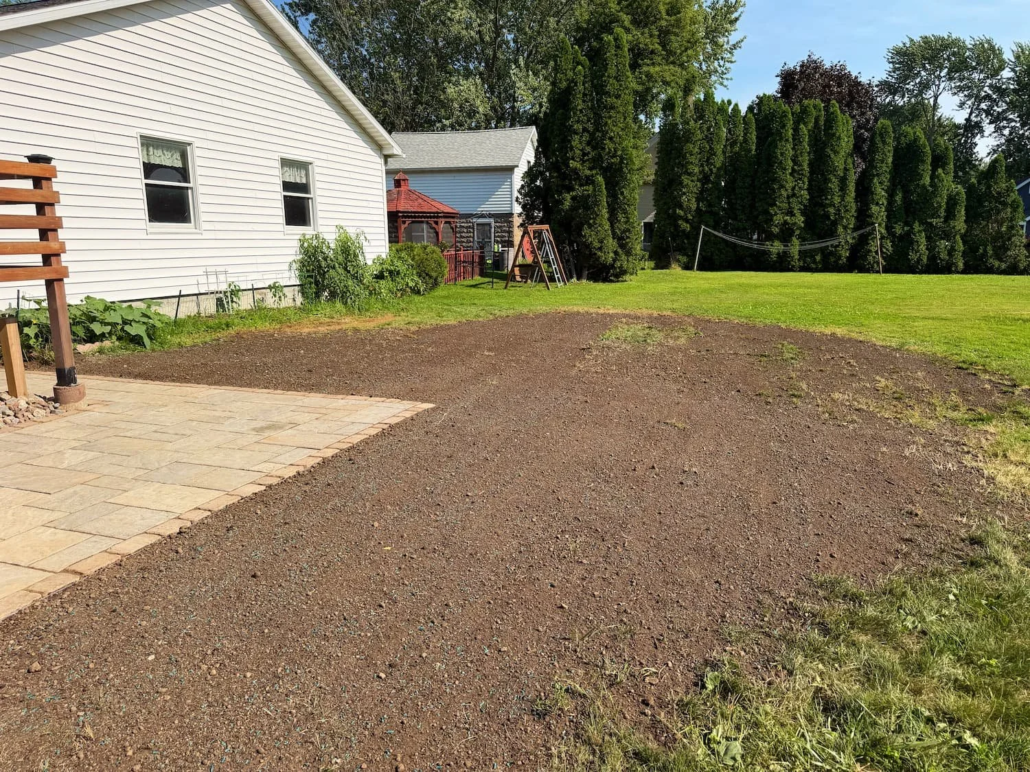 Completed landscaping with planted beds surrounding a wood deck in a Central New York backyard.