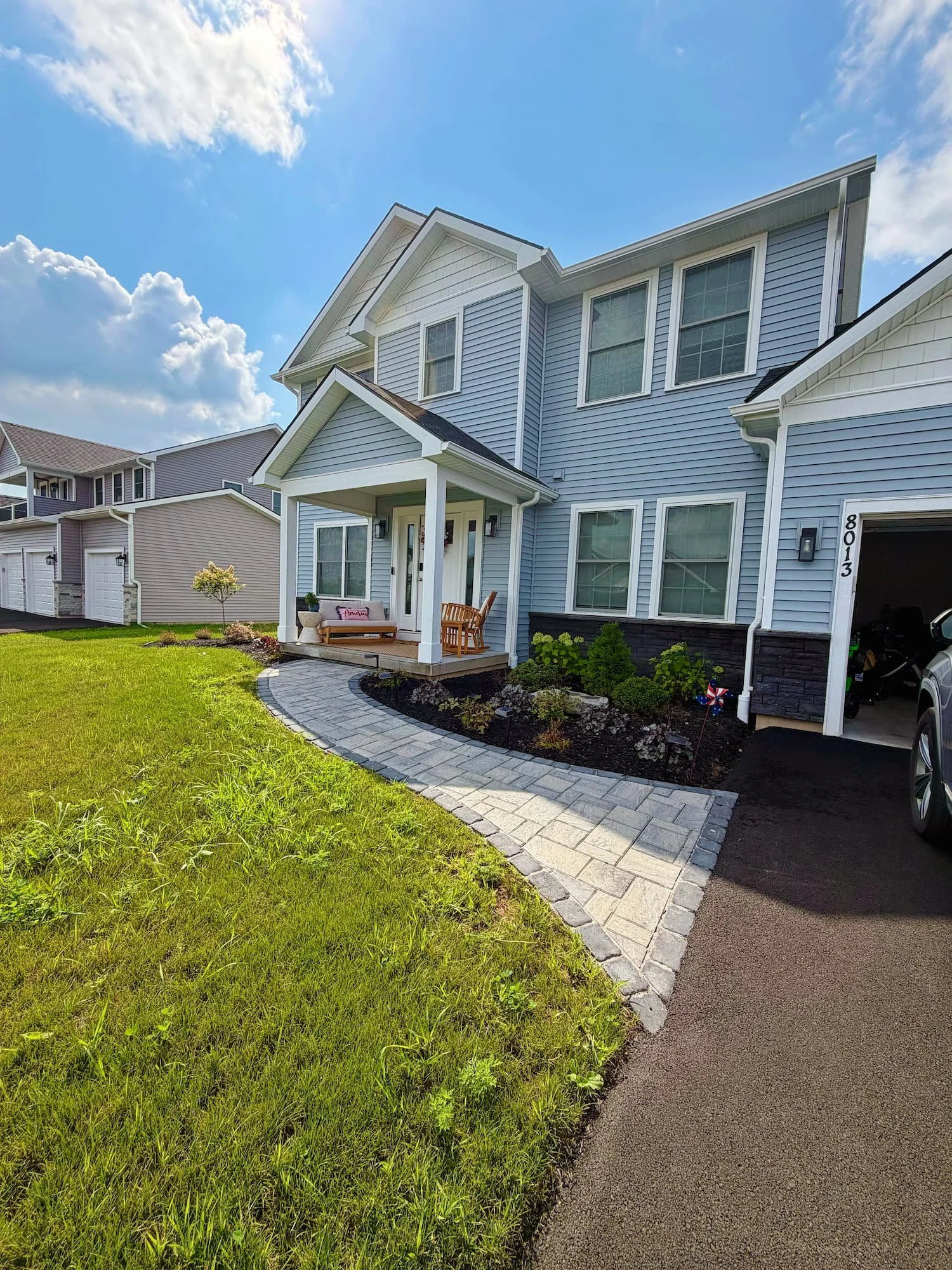Landscaped front planting bed with shrubs, perennials, dark mulch, and a paver walkway in Central NY.