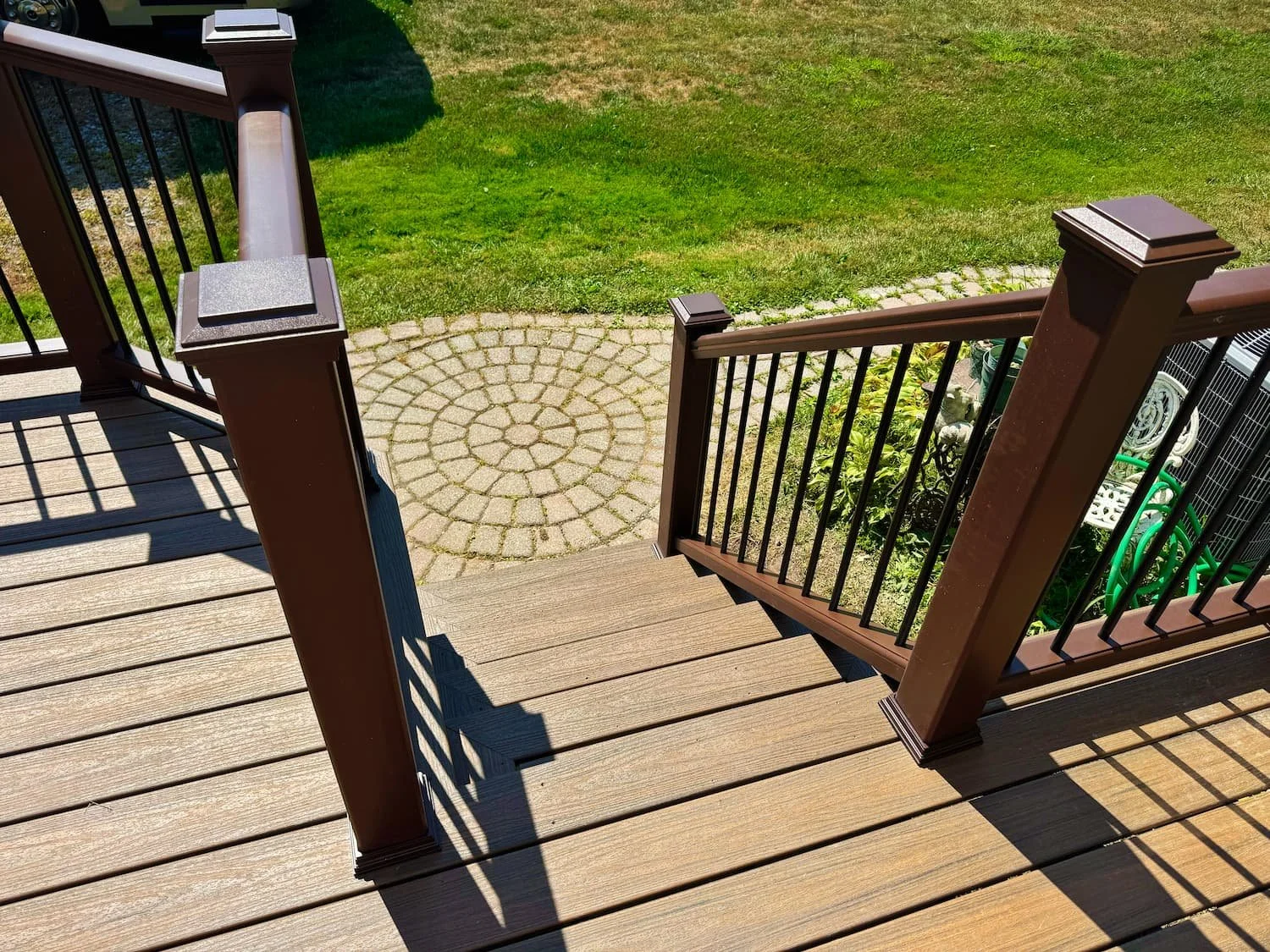 Custom composite deck with brown and black railing beside an existing paver walkway in Central NY