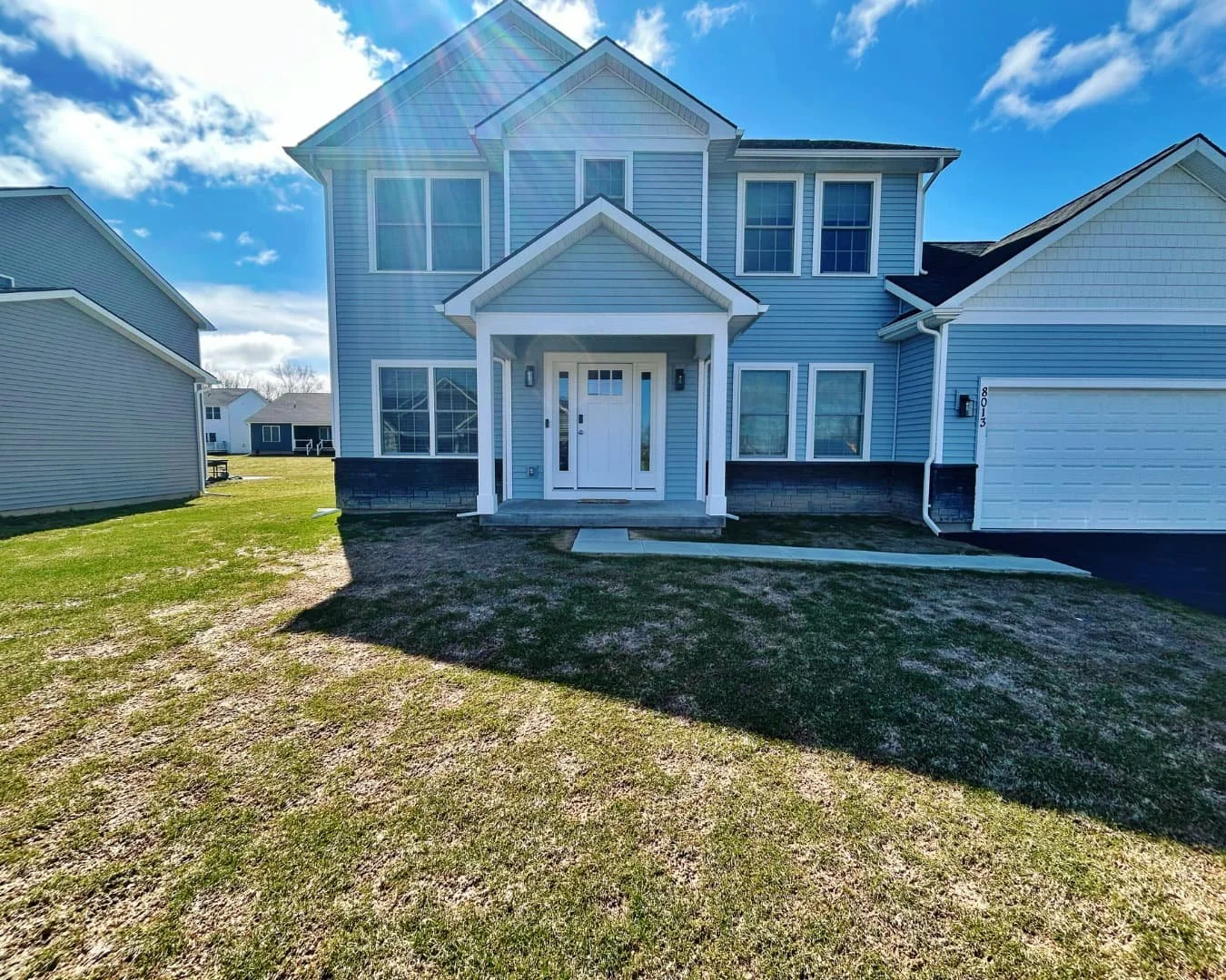 Front entrance of a two-story blue house before landscaping improvements, with a covered porch, white front door, concrete walkway.
