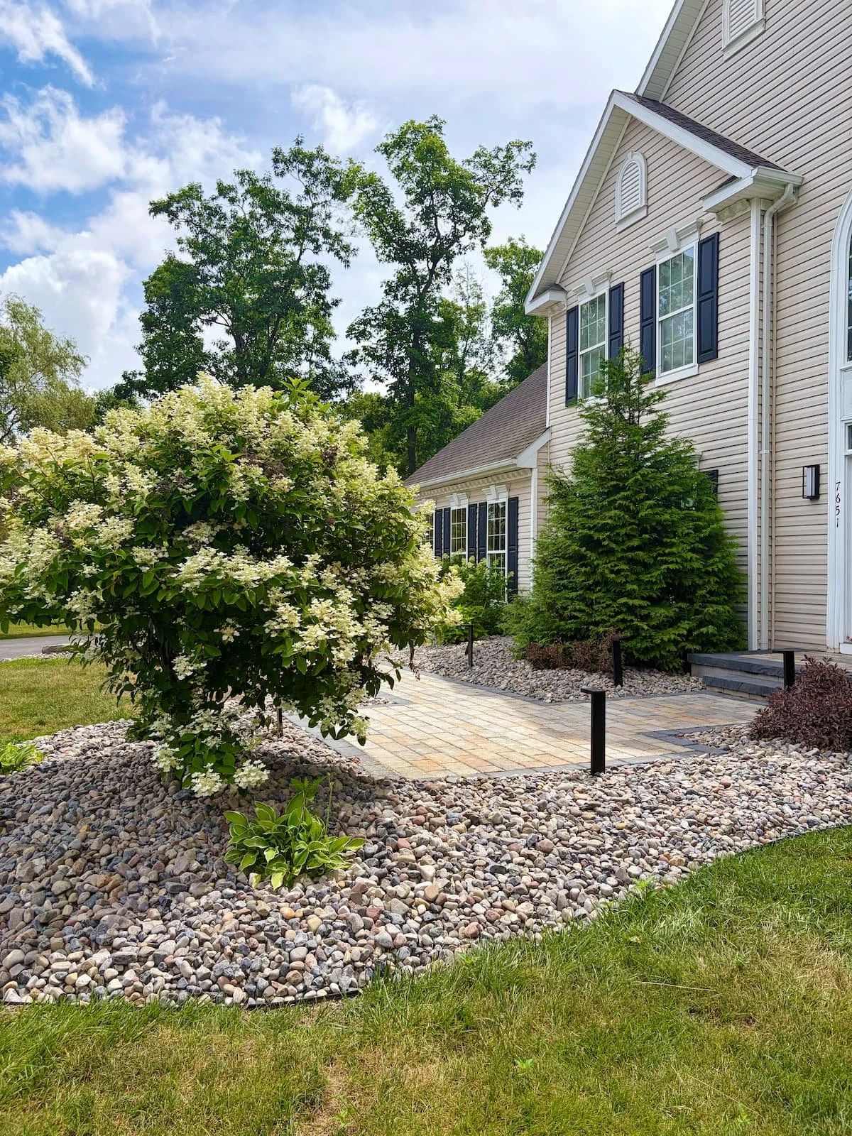 Modern paver and landscape installation with shrubs and decorative stone along a Central NY home.