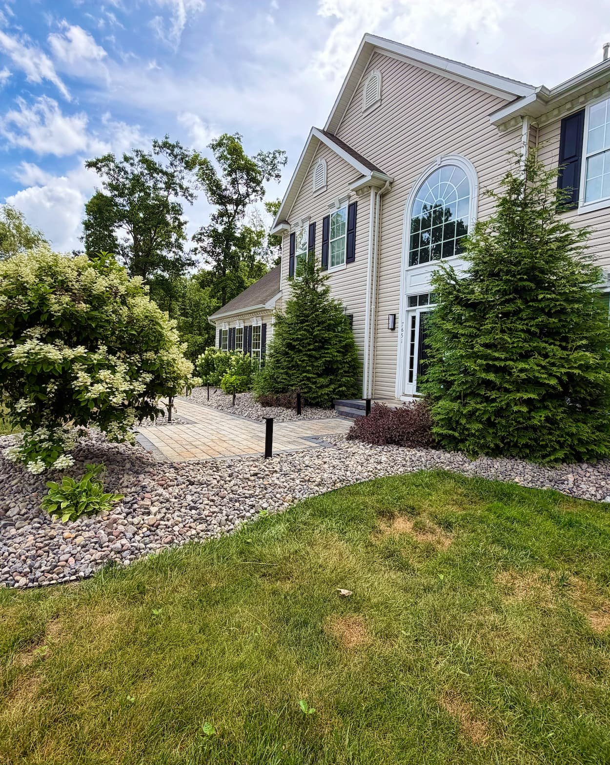 Decorative river rock landscape bed with shrubs and plantings along a Central NY home.