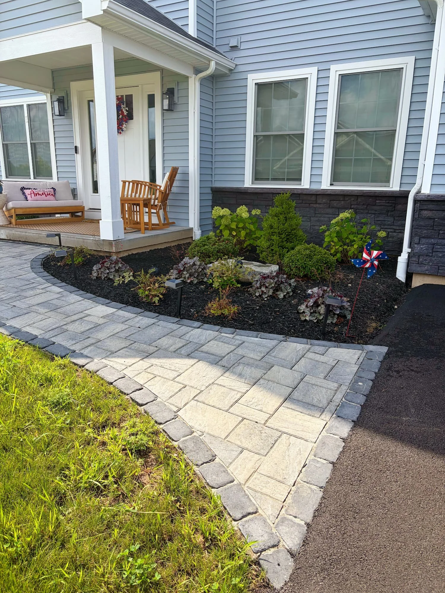 Curved paver walkway bordered by professionally designed front yard landscaping in Central NY