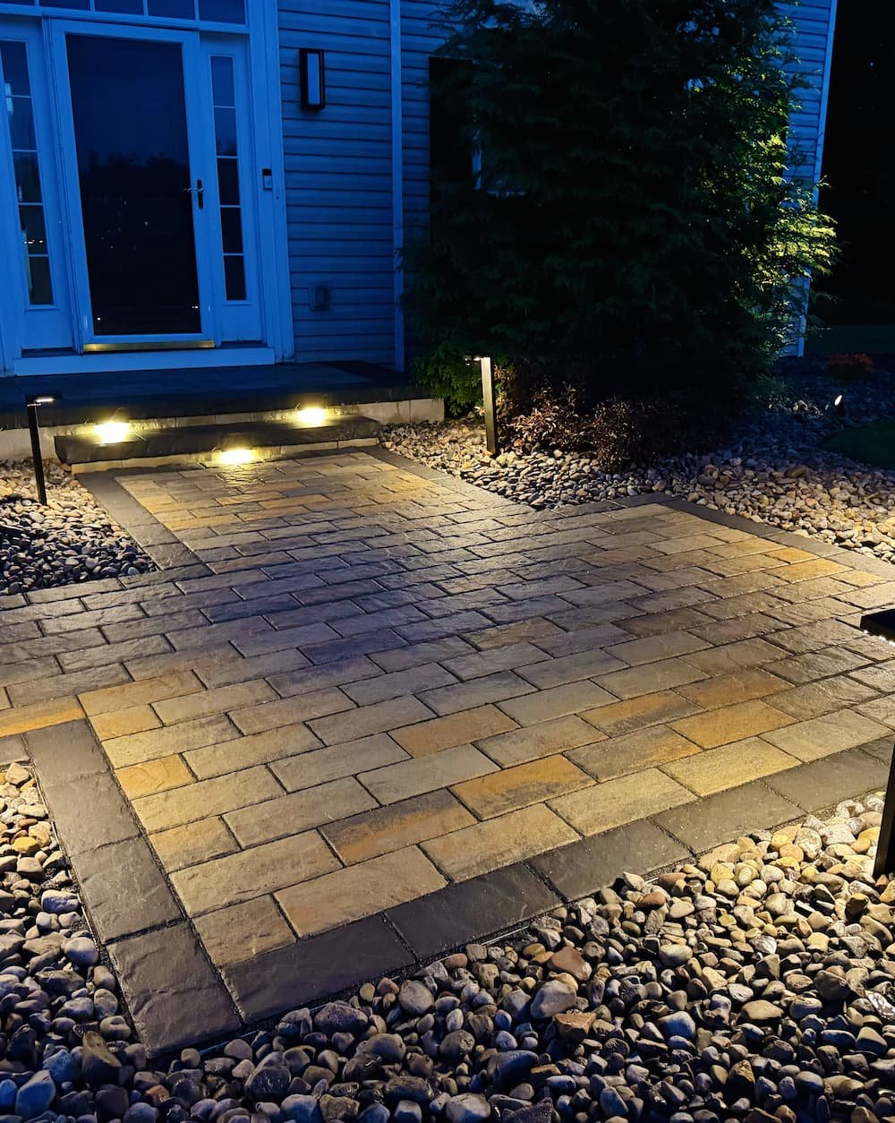 Landscape lighting illuminating a custom paver walkway designed by Pines and Pavers in Central NY.