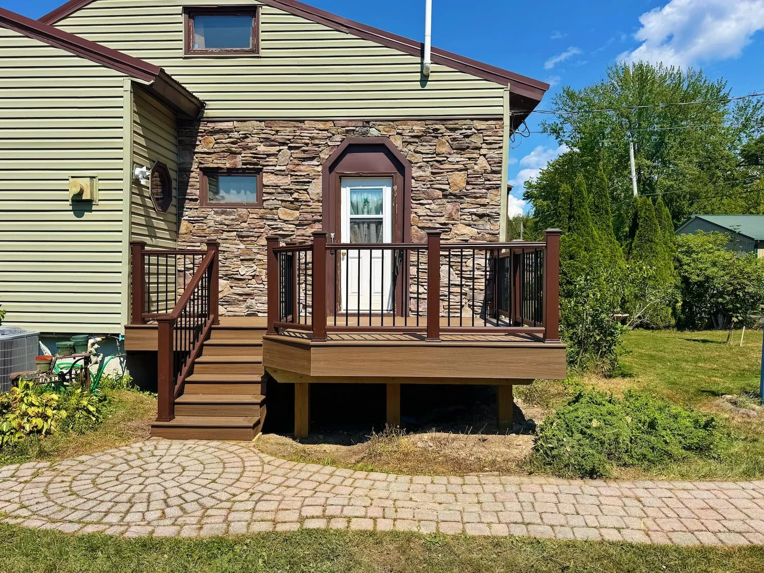 Composite deck stairs with brown railing leading to an existing paver walkway in Central New York