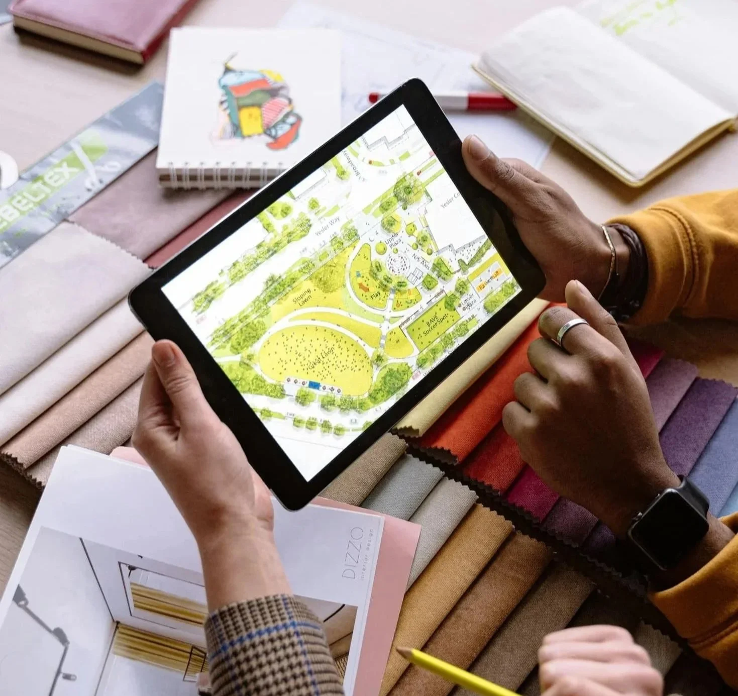 Landscape design planning session with a digital backyard layout displayed on a tablet surrounded by material samples and design inspiration for a custom outdoor living project.