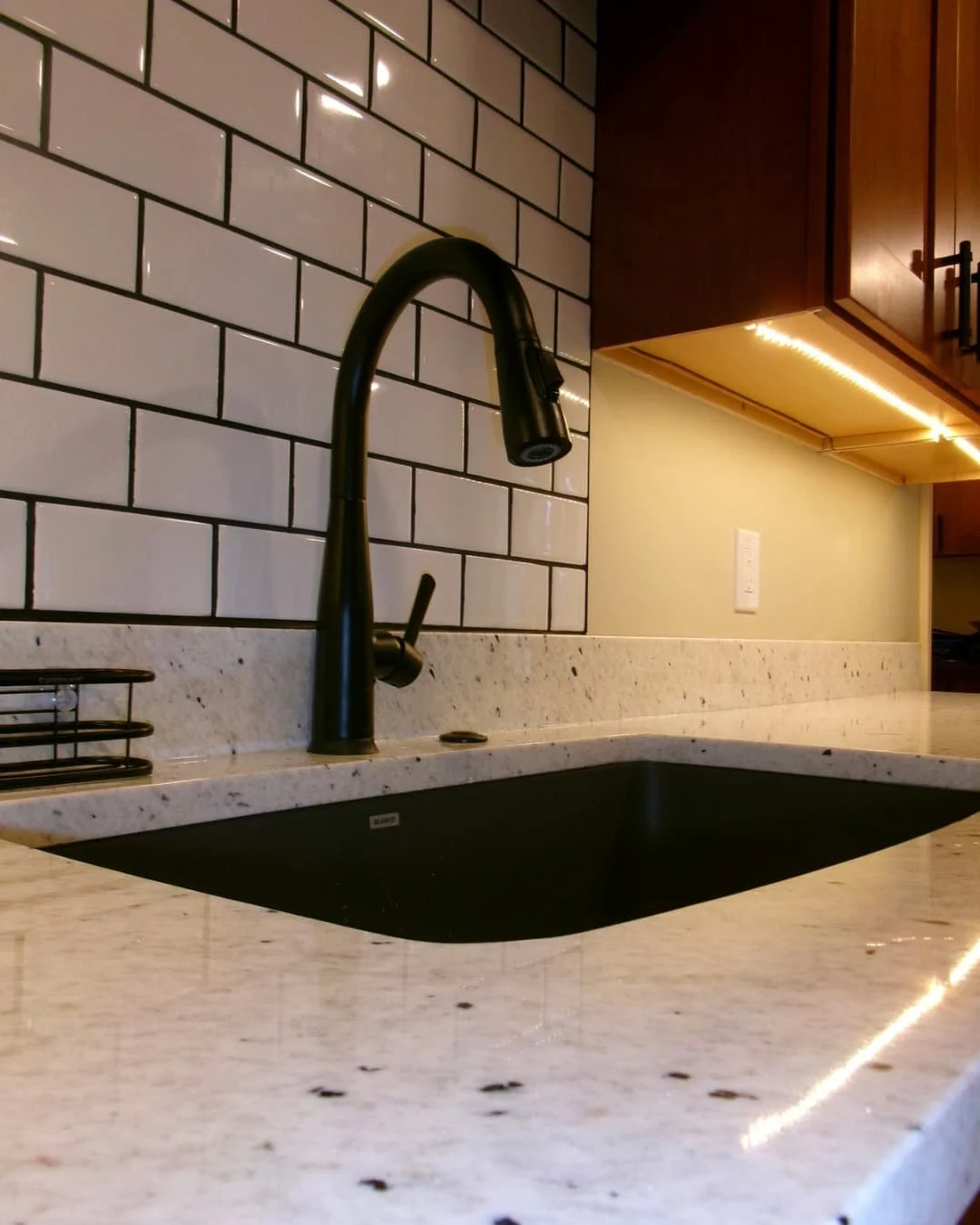 Kitchen faucet and backsplash detail in an Upstate New York remodel with granite countertops and dark sink fixtures.
