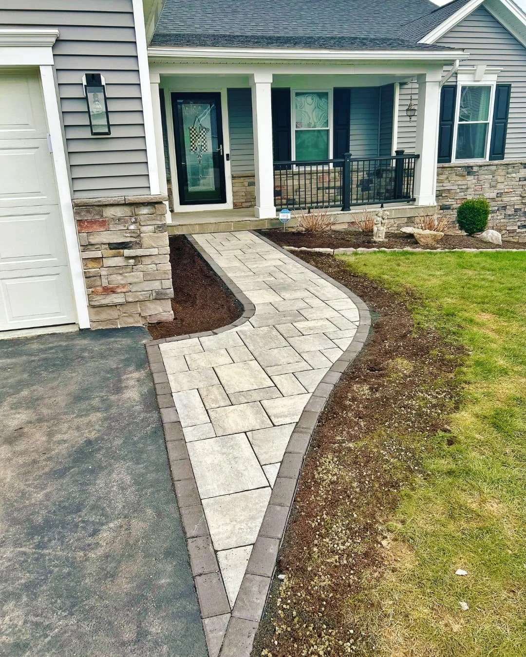 Front entrance of a two-story blue house before landscaping improvements, with a covered porch, white front door, concrete walkway.