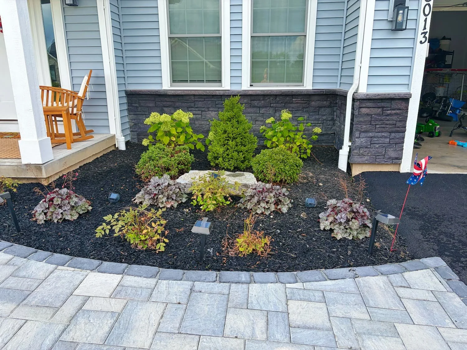 Front yard planting bed featuring shrubs, colorful perennials, decorative stone, and dark mulch in Central NY.