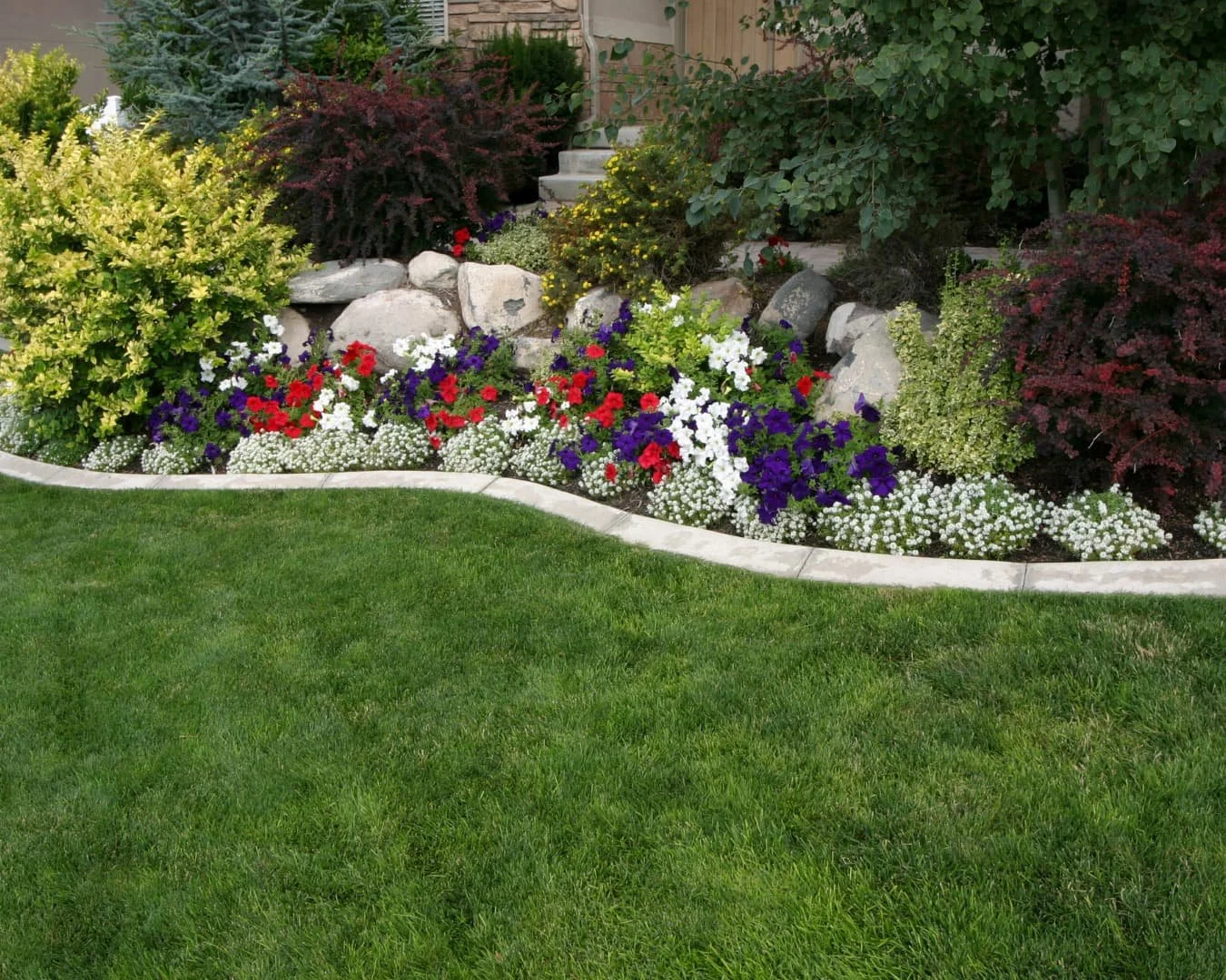 Layered landscaping inspiration with foundation planting, stone edging, and varied shrub heights for a structured look.