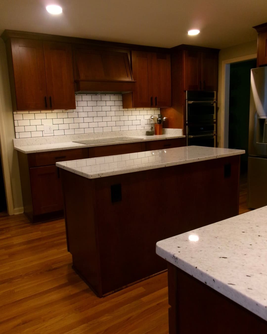 Kitchen island overview in a Central New York renovation with granite counters, updated cabinets, and wood flooring.