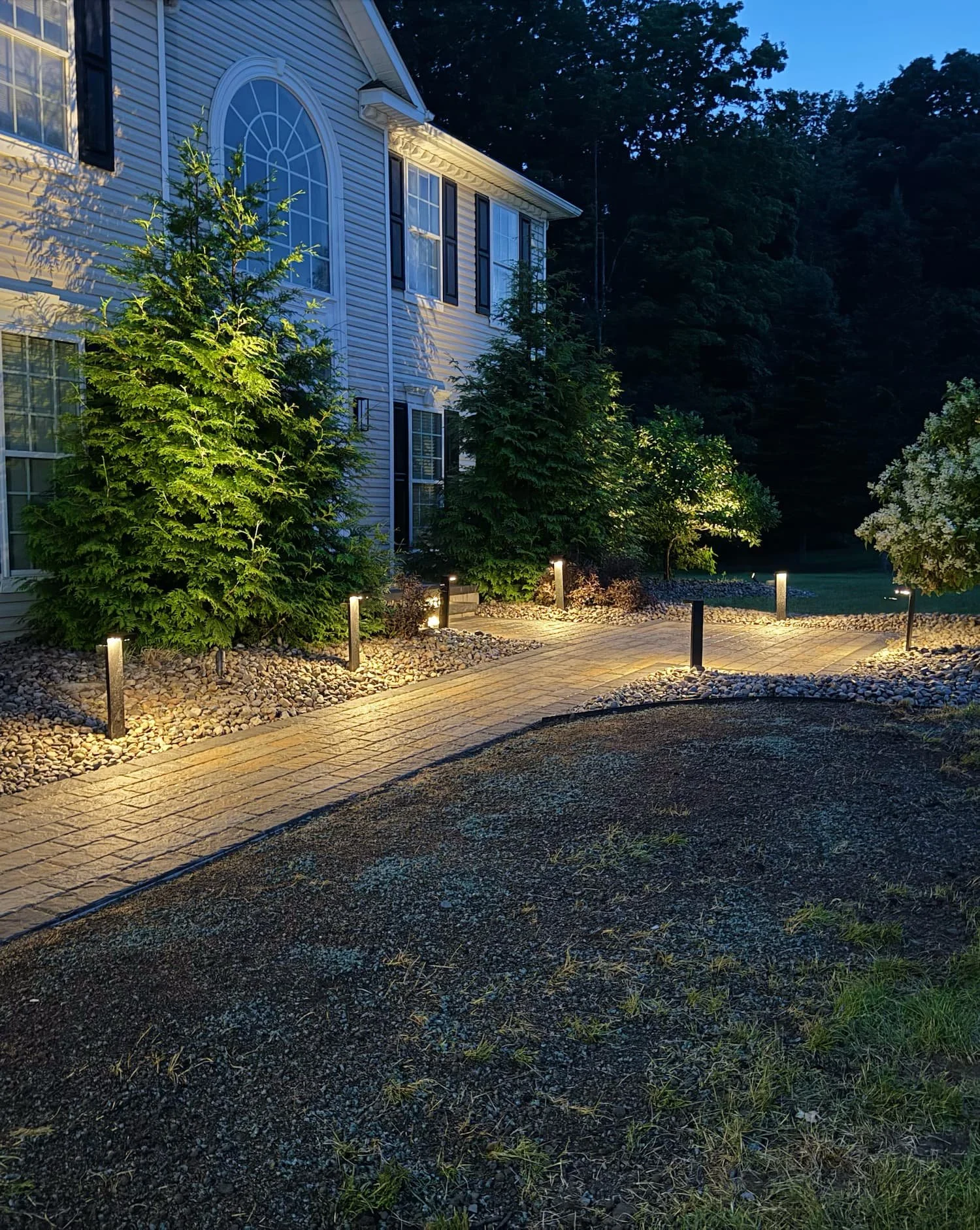 Paver walkway illuminated by warm landscape lighting for a Central NY residential property.