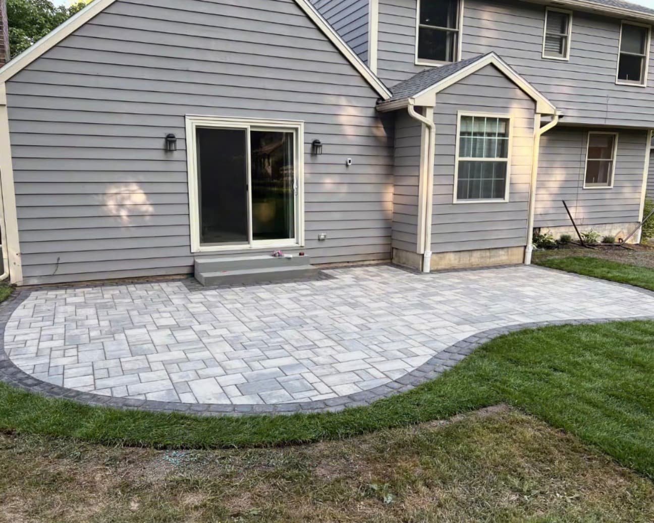 Curved backyard paver patio at a Camillus, NY home with gray stone pavers and a clean finished edge.