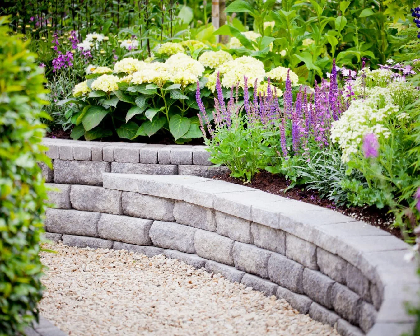 Raised garden bed inspiration with stacked stone edging and colorful flowering plants.