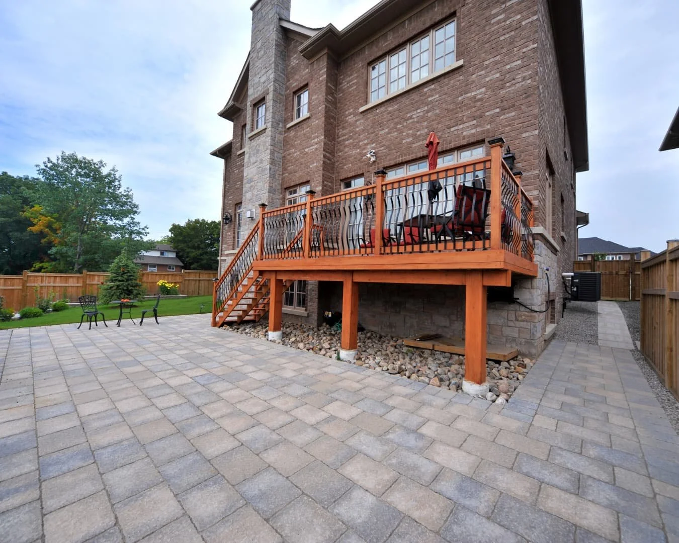 Elevated deck inspiration attached to a brick home with steps leading down to a paved backyard area.