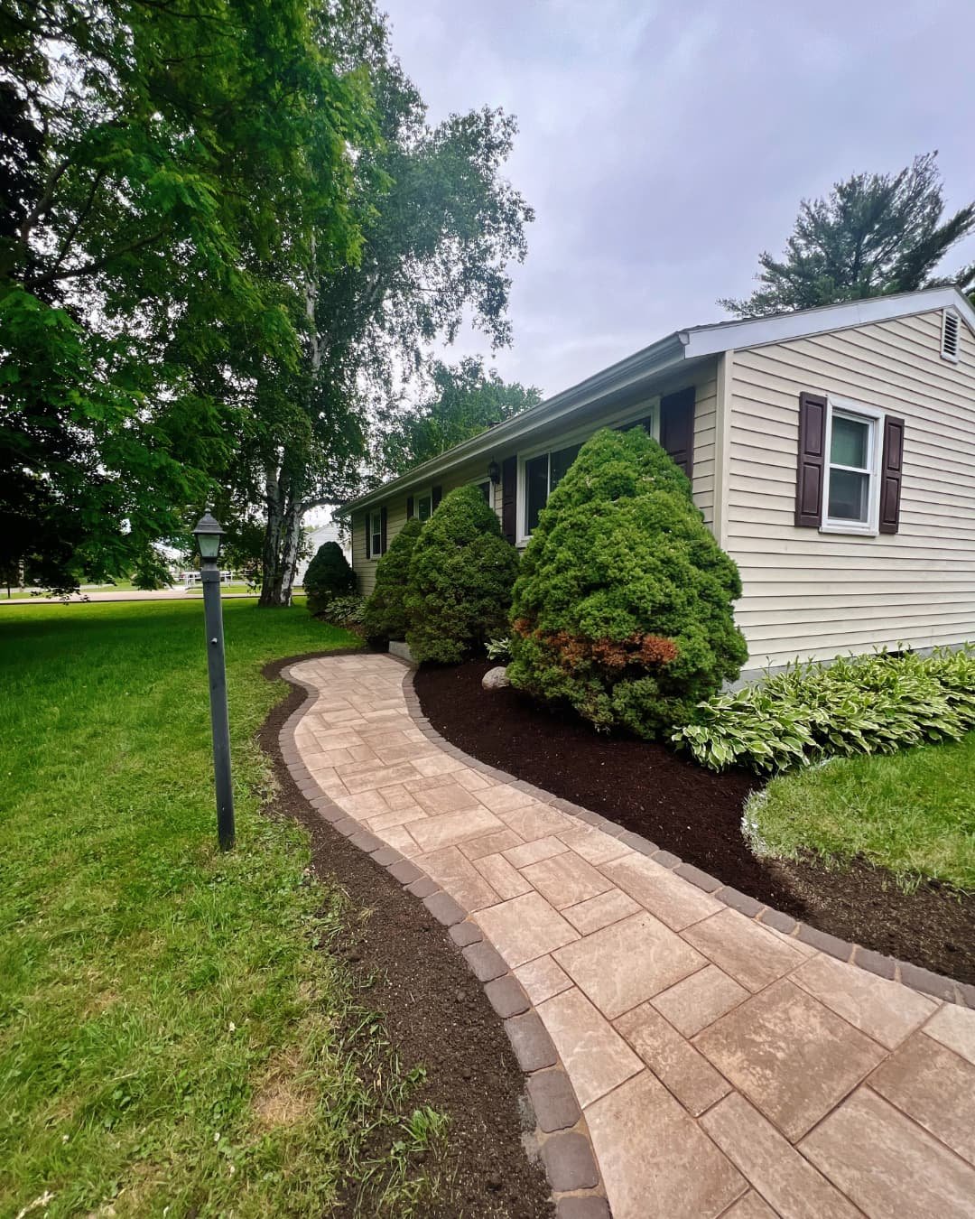 Landscape bed and curved walkway beside the home completed by Pines and Pavers in Central New York.